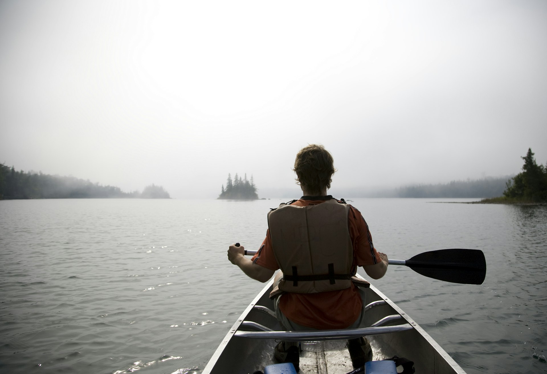 looking from behind me see a man in a canoe paddling across a misty lake near Isle Royale