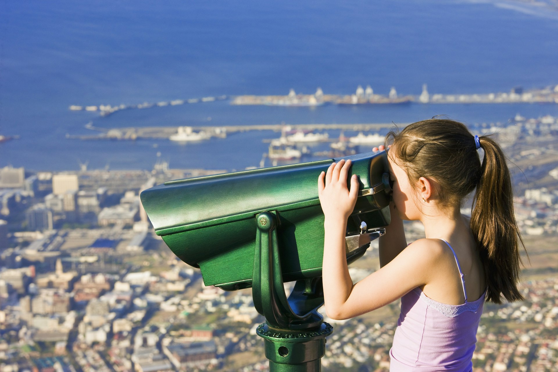 Young white girl looking out over Cape Town through binoculars at the top of Table Mountain, South Africa