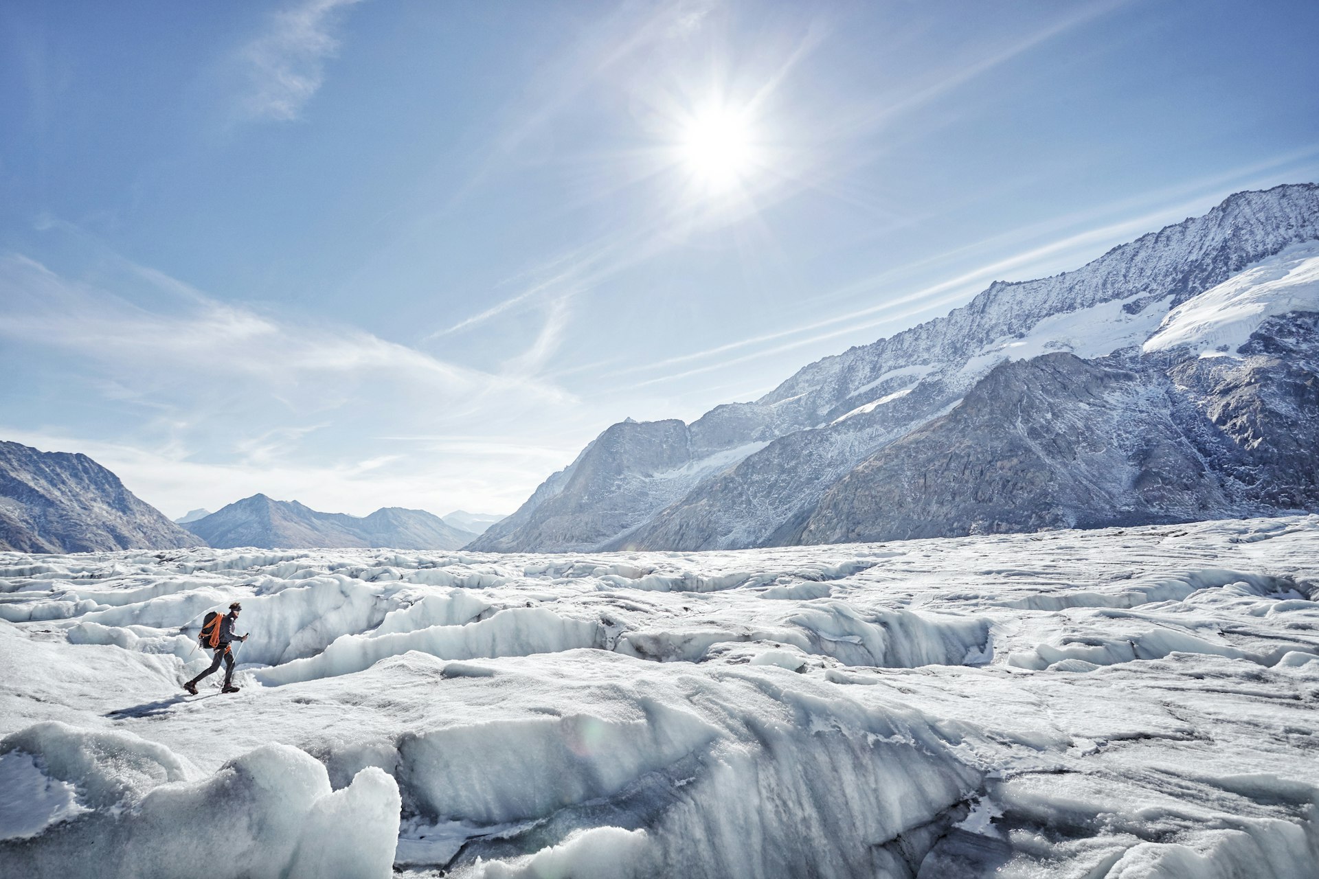 A person hikes on a vast glacier as the sun shines down