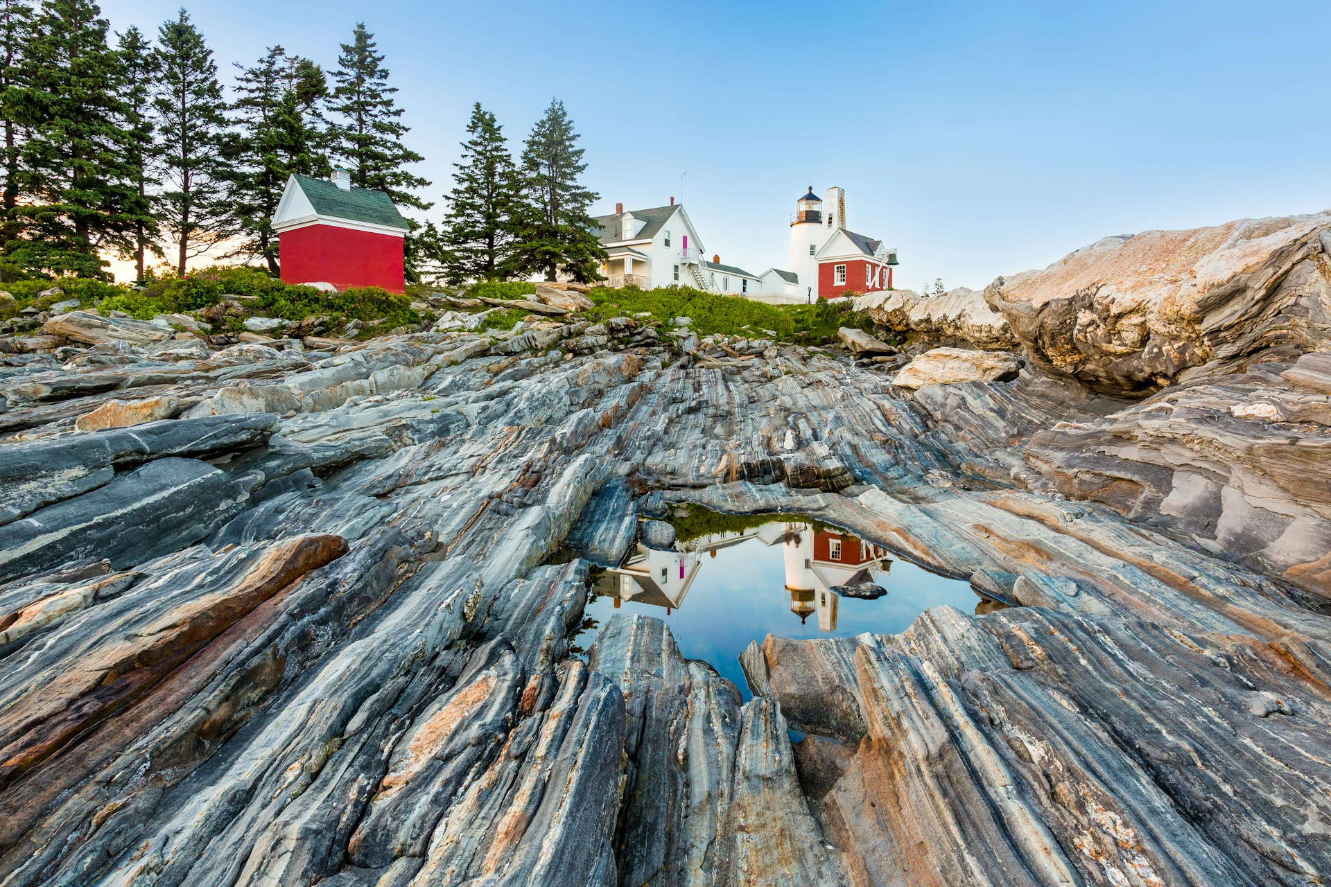 The characteristic "gneiss" rocks along the coast of the Pemaquid Peninsula allows for water to form in recesses. The lighthouse is reflected on this water surface. The Pemaquid Point Light is a historic U.S. lighthouse located in Bristol, Lincoln County, Maine, at the tip of the Pemaquid Neck