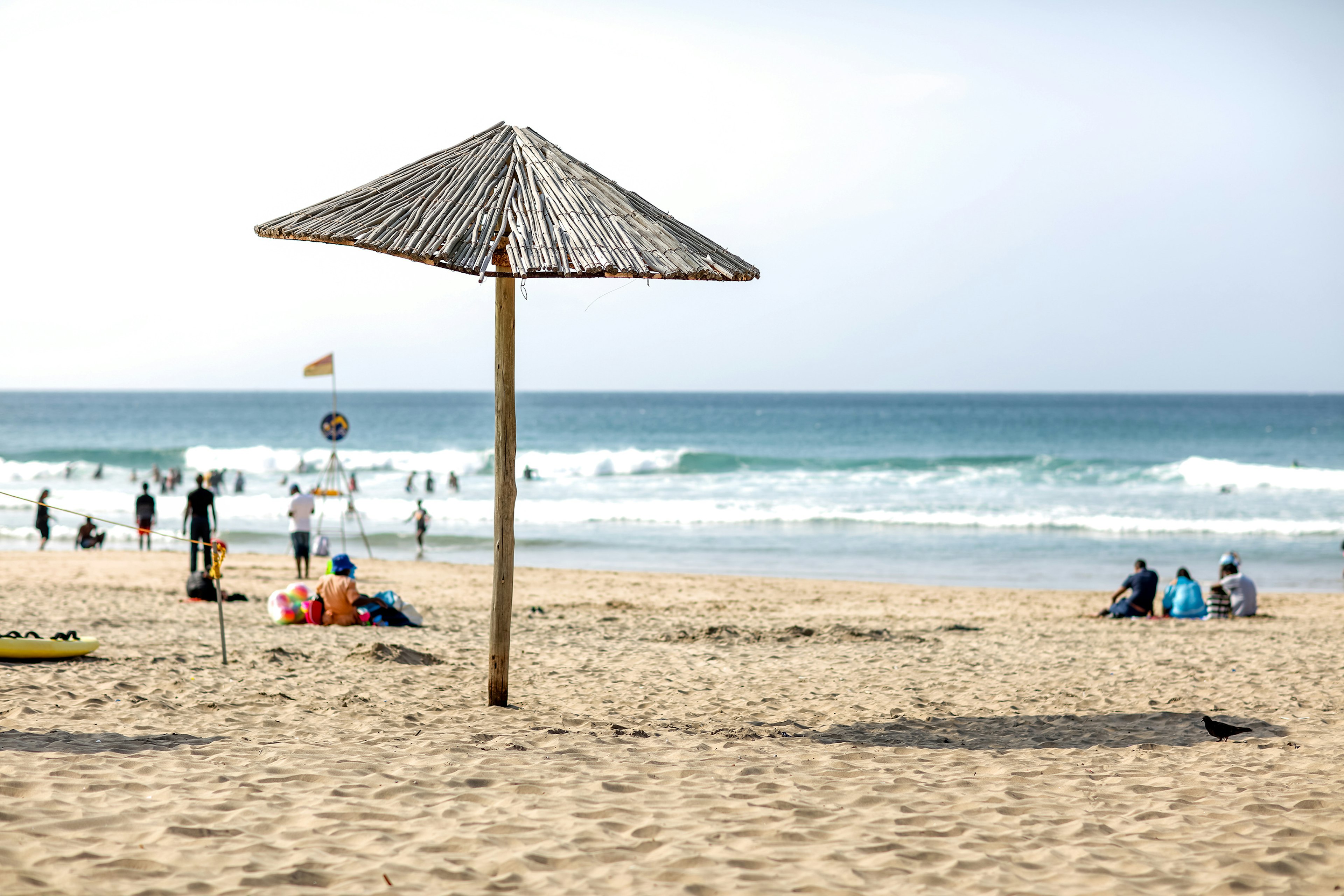 A sandy beach with a sunshade and several people relaxing or splashing in the surf