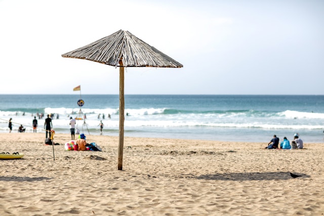 A sandy beach with a sunshade and several people relaxing or splashing in the surf