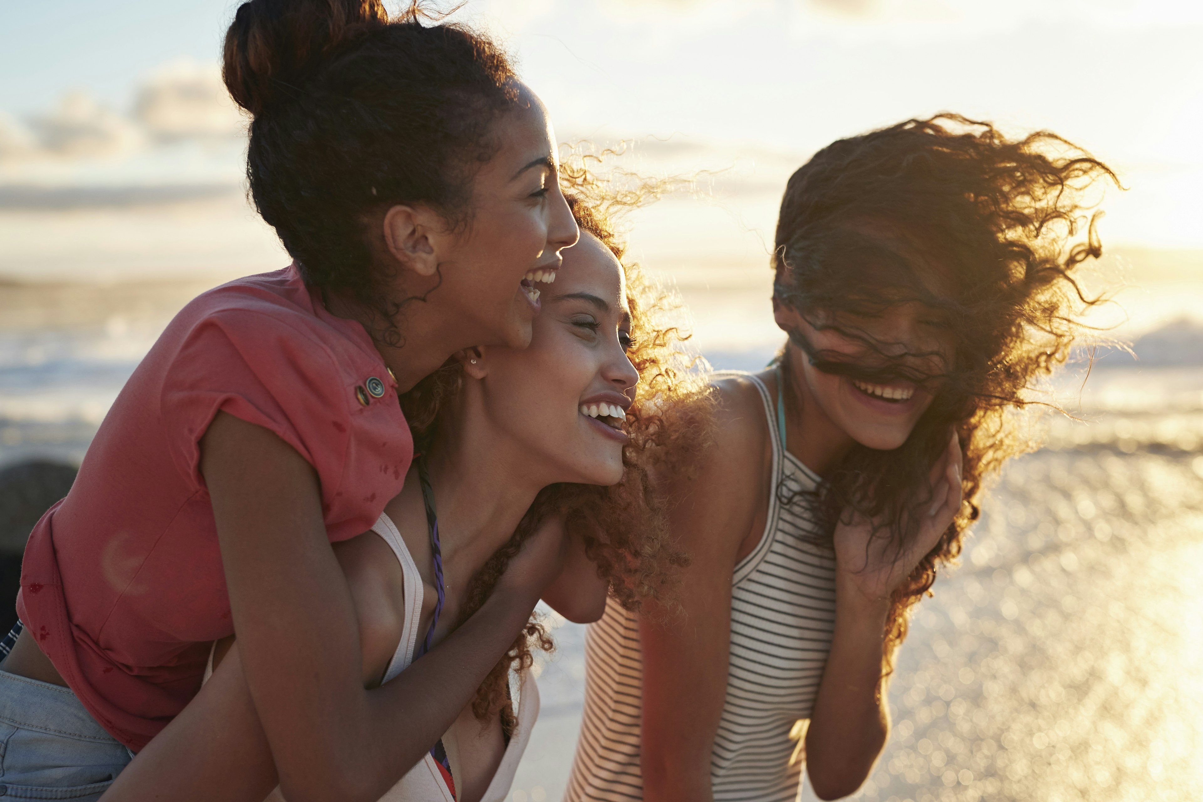 Three young laughing women hanging out at a Cape Town beach during sunset