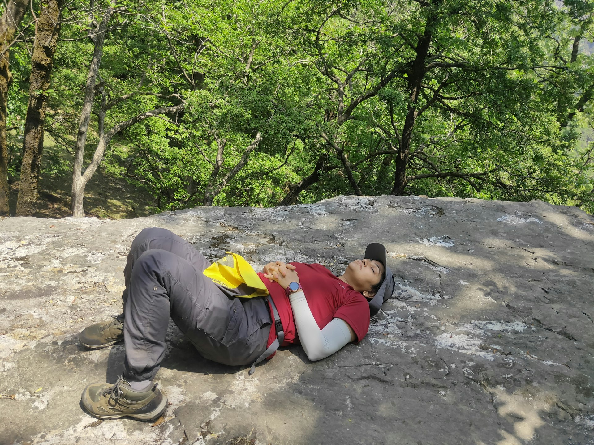 An Indian hiker lays on her back with her eyes shut on top of a rock to think
