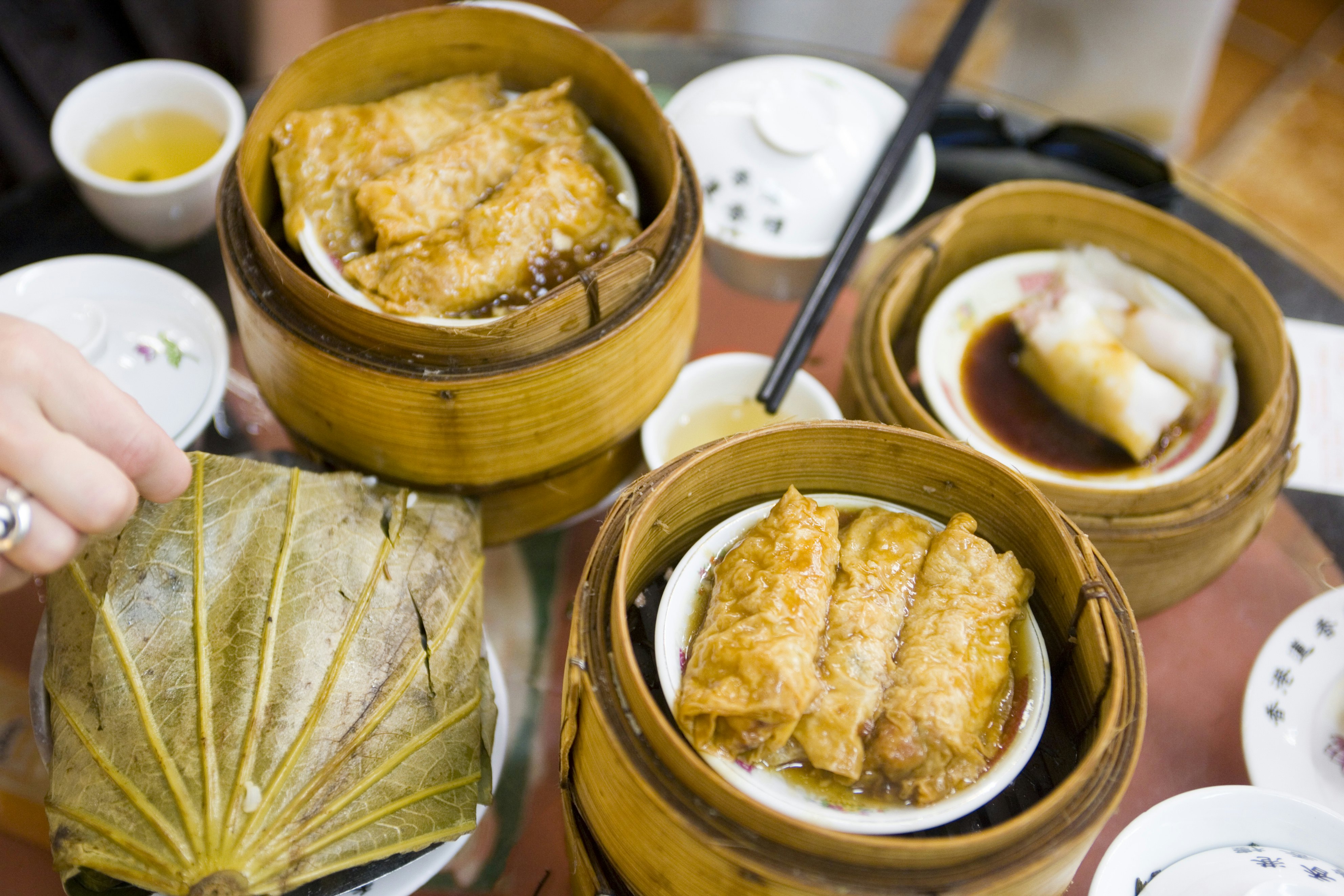 Round wicker baskets hold small dainty dumplings. A hand holding chopsticks reaches over to take some