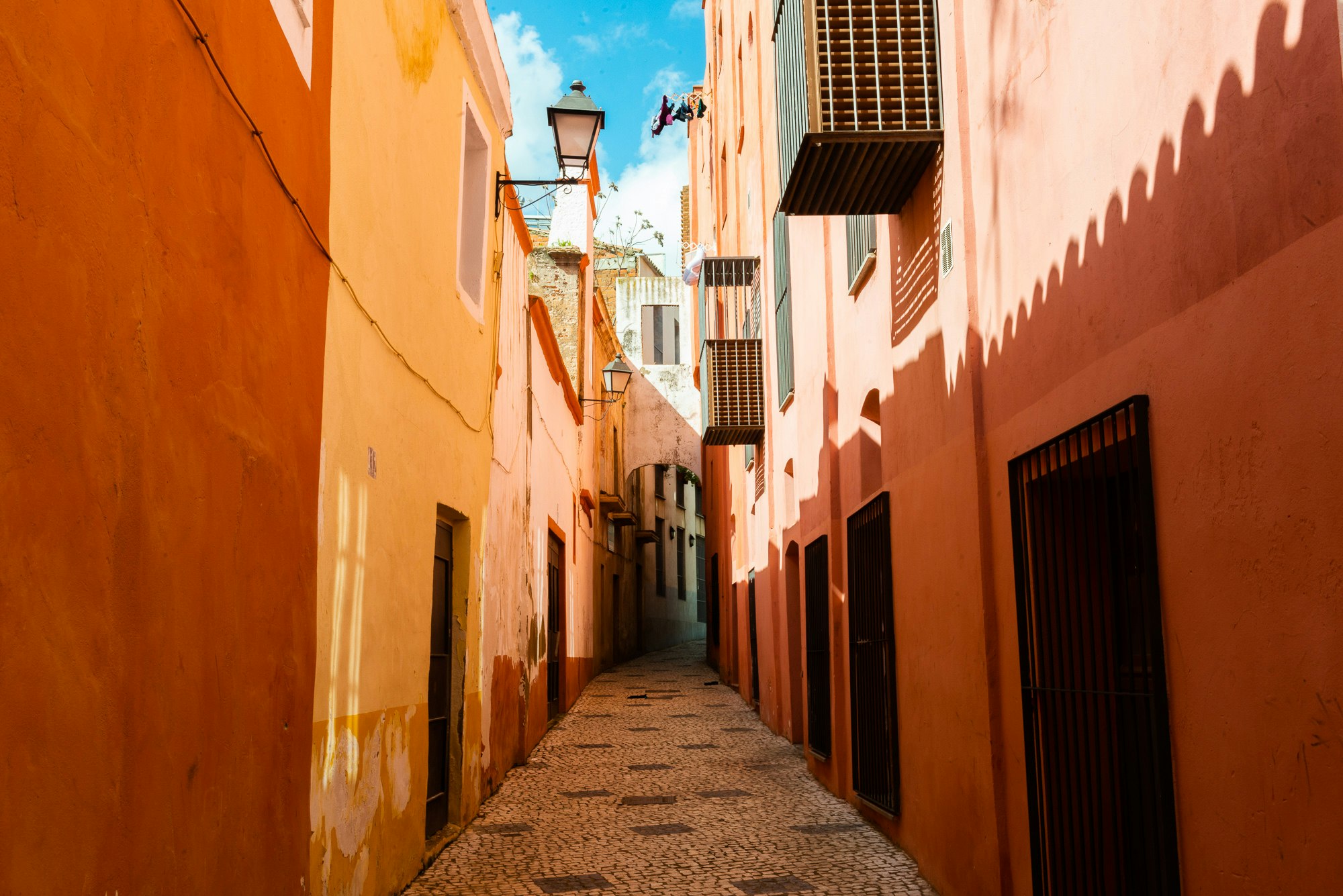 Una calle estrecha con edificios pintados en naranjas, amarillos y rosas, Badajoz, Extremadura, España