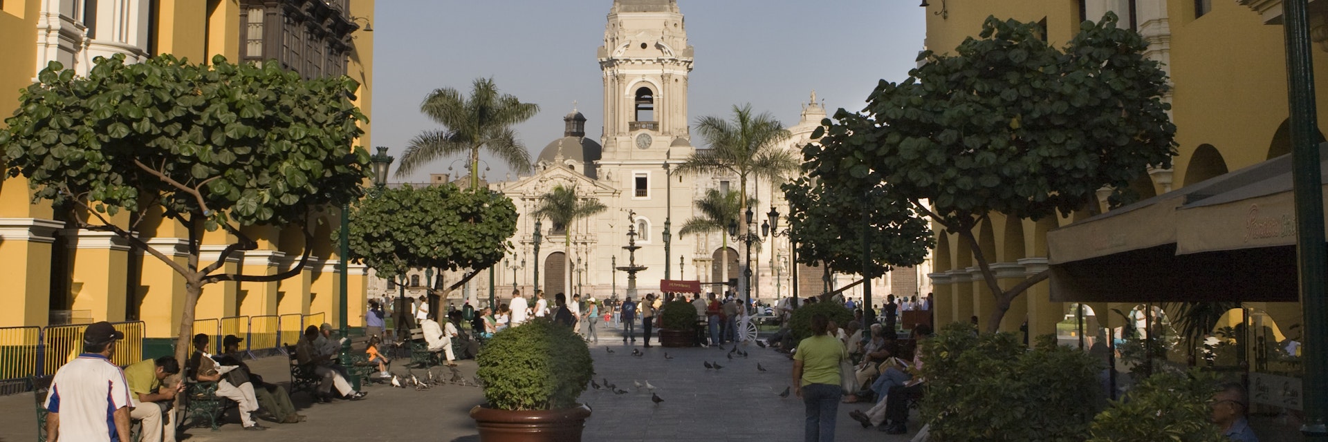 People walk down the colorful Pasaje Santa Rosa in Lima, Peru with the Municipal Palace and art gallery on the left, a restaurant on the right and the Plaza de Armas and Cathedral of Lima in the distance.
905328568