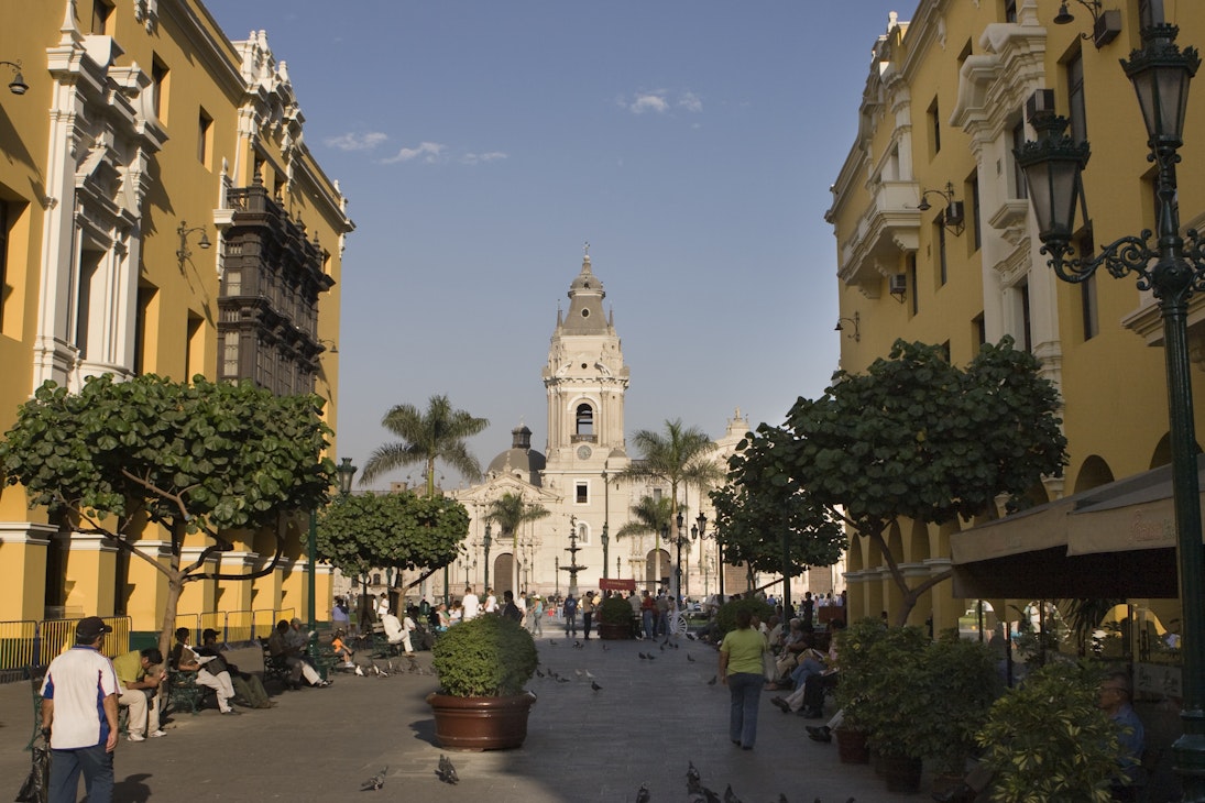People walk down the colorful Pasaje Santa Rosa in Lima, Peru with the Municipal Palace and art gallery on the left, a restaurant on the right and the Plaza de Armas and Cathedral of Lima in the distance.
905328568