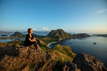 Scenic view with resting female pansian hiker on Padar island Komodo National Park, Indonesia. The mountainous seascape in Indonesia is famous for its incredible vistas.