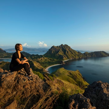Scenic view with resting female pansian hiker on Padar island Komodo National Park, Indonesia. The mountainous seascape in Indonesia is famous for its incredible vistas.