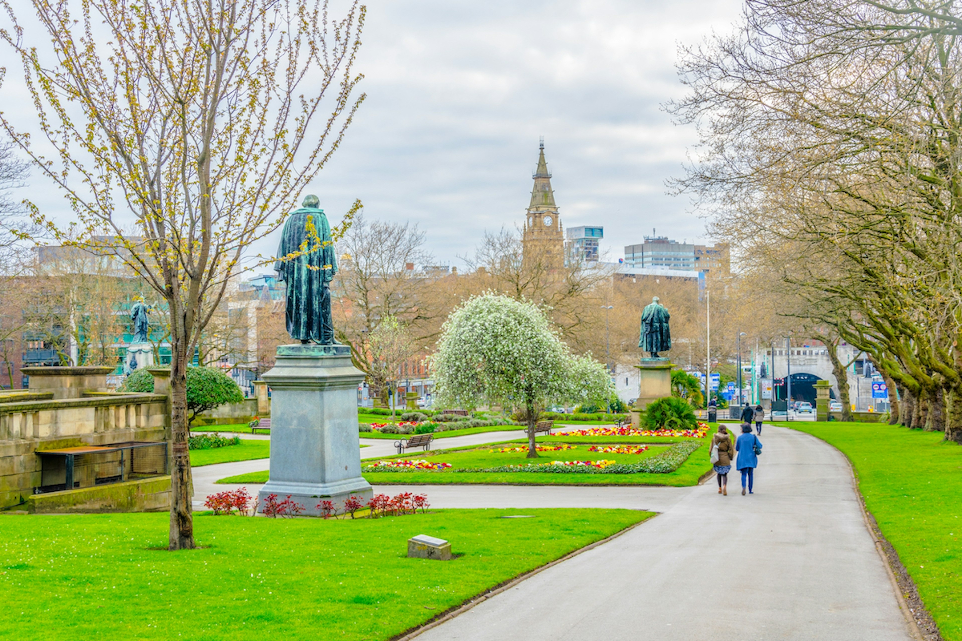 People walk through a park in Liverpool on a grey and rainy day.