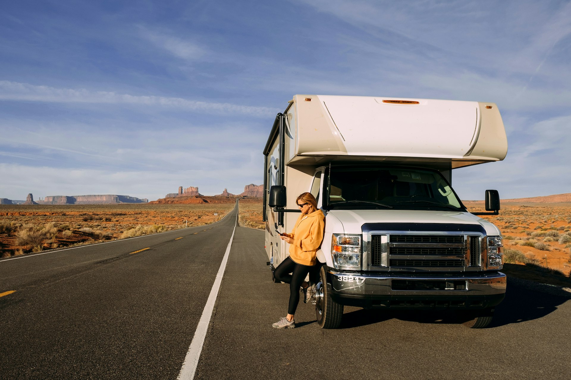 A woman travels by motorhome through Monument Valley in the USA desert and checks her mobile phone parked on the side of the road.