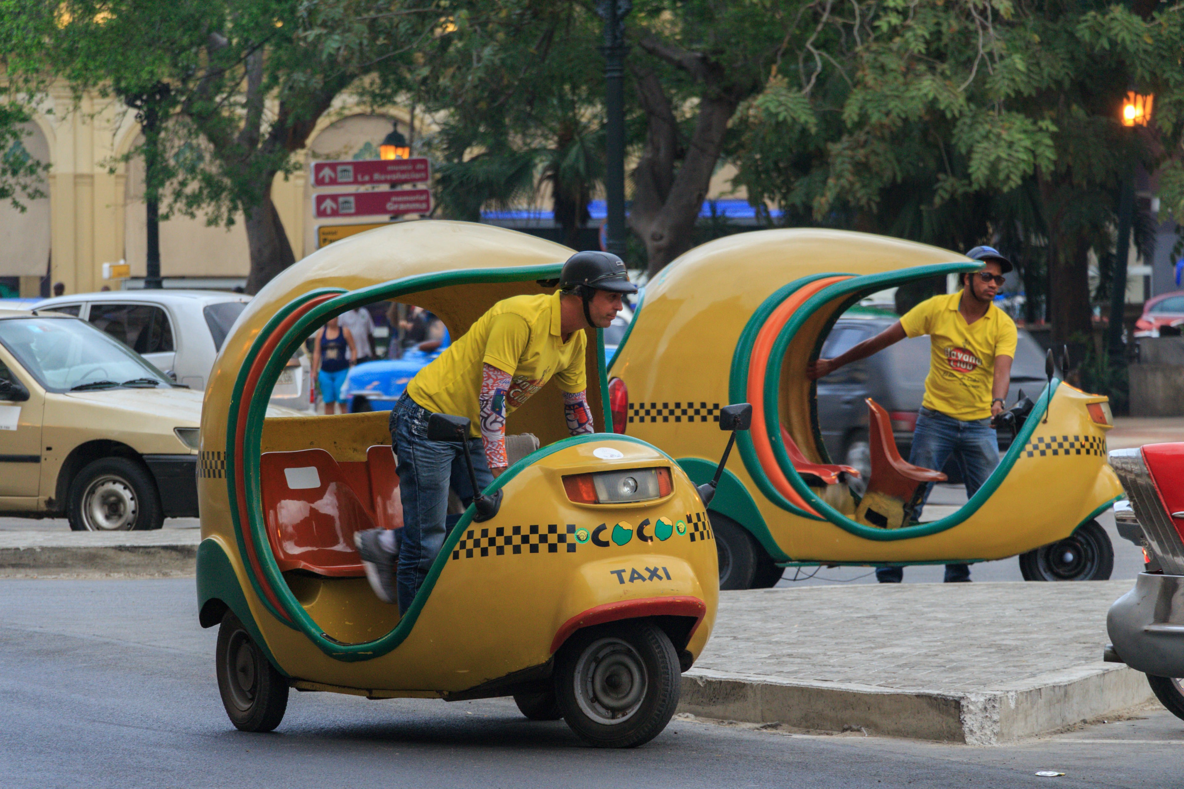 Two taxi drivers with yellow scooter taxis (bici-taxis) in Old Havana.