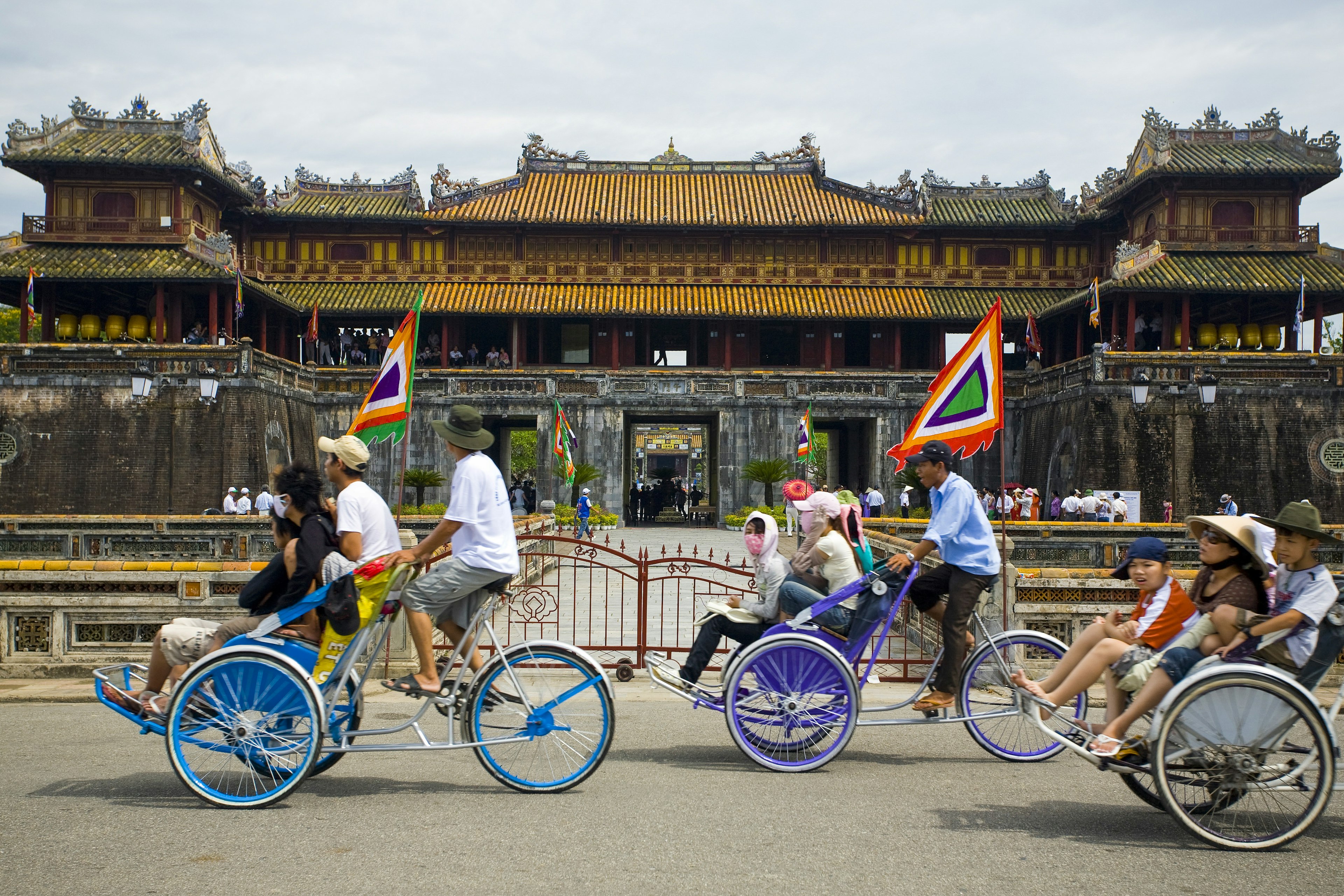 People sat in the front of pedal-powered rickshaws pass an ancient temple