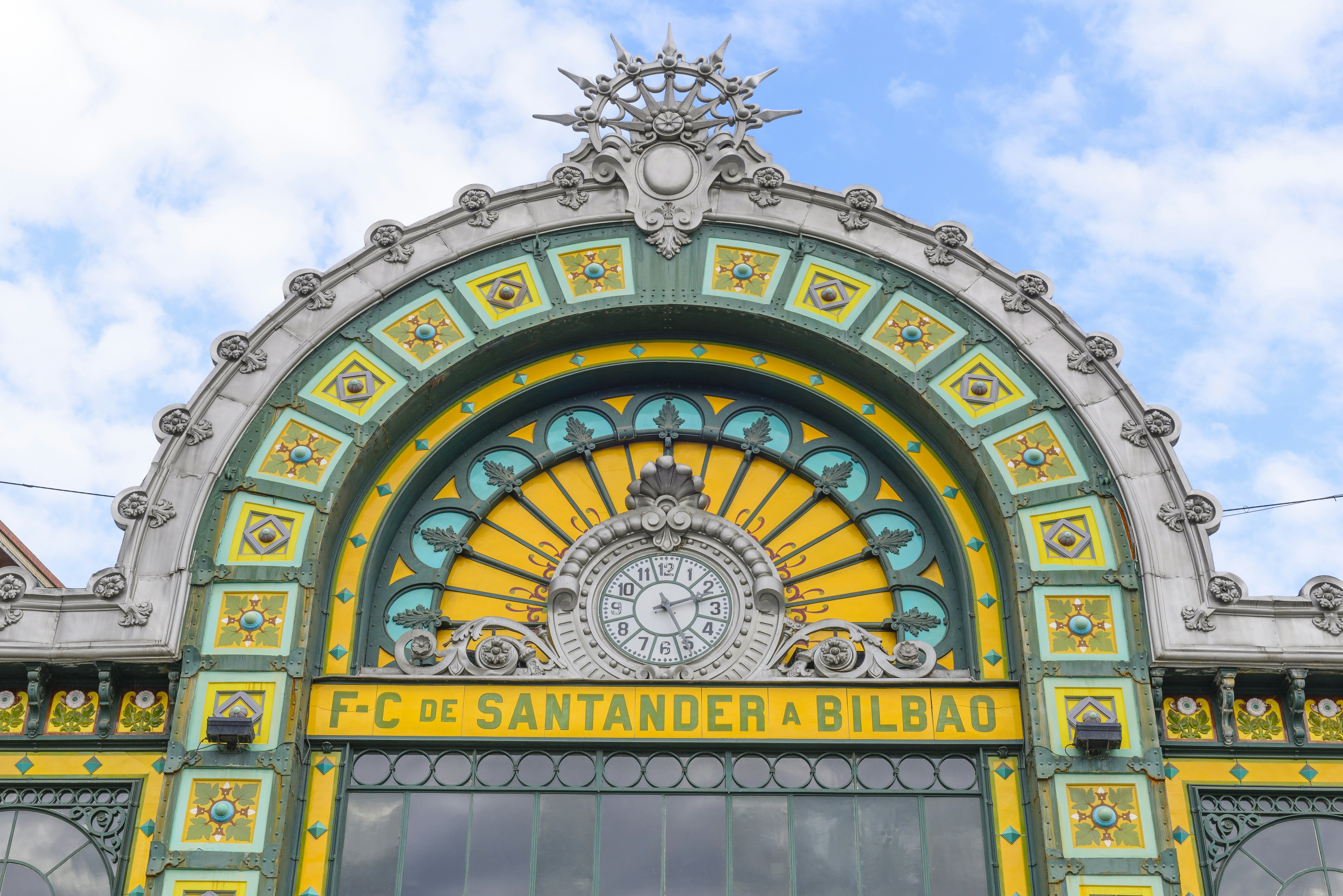 Ornate exterior of a train station with yellow and green tilework around a clock.