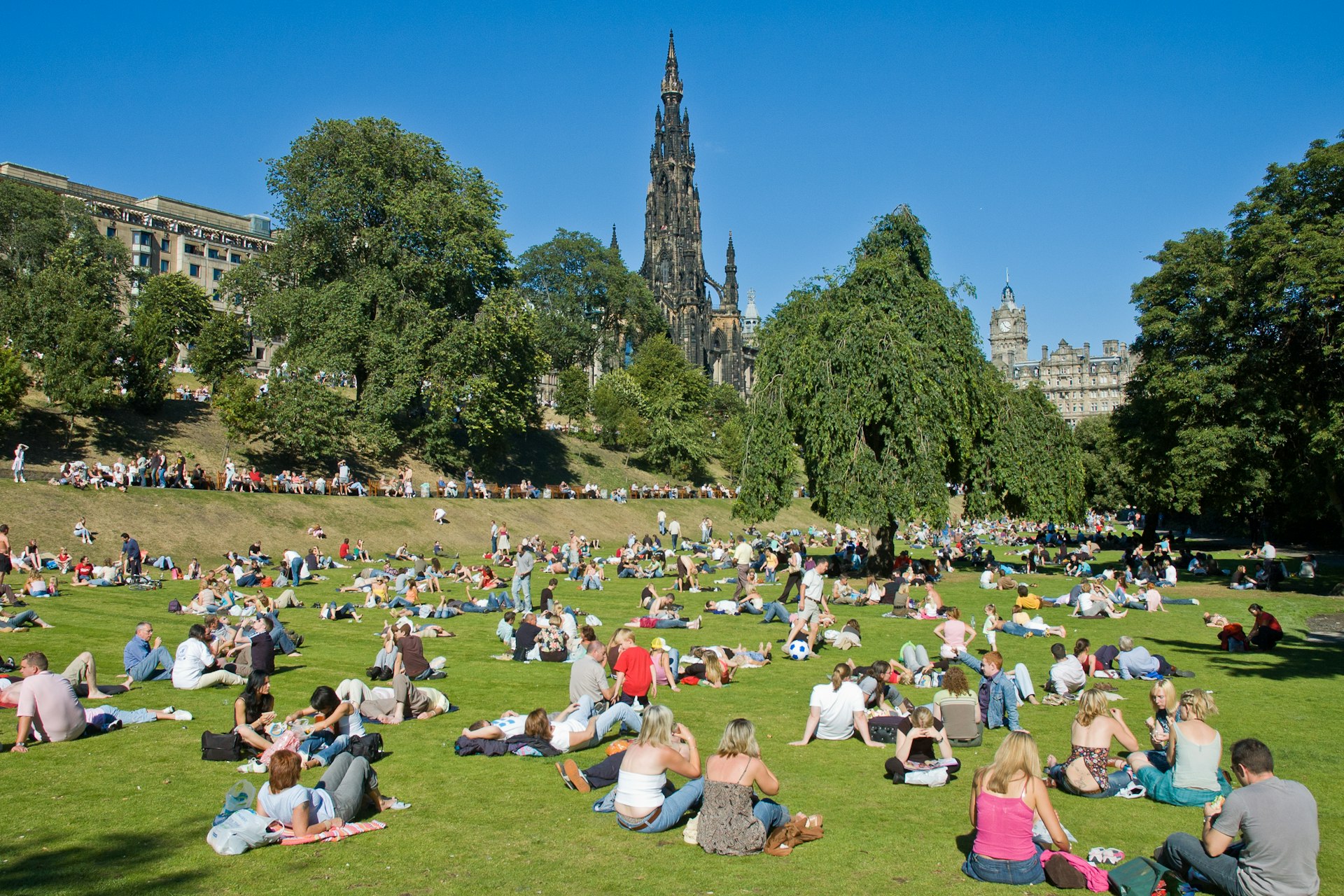 The Princes Street Gardens full of people with the Scott Monument behind on a sunny summer day. 