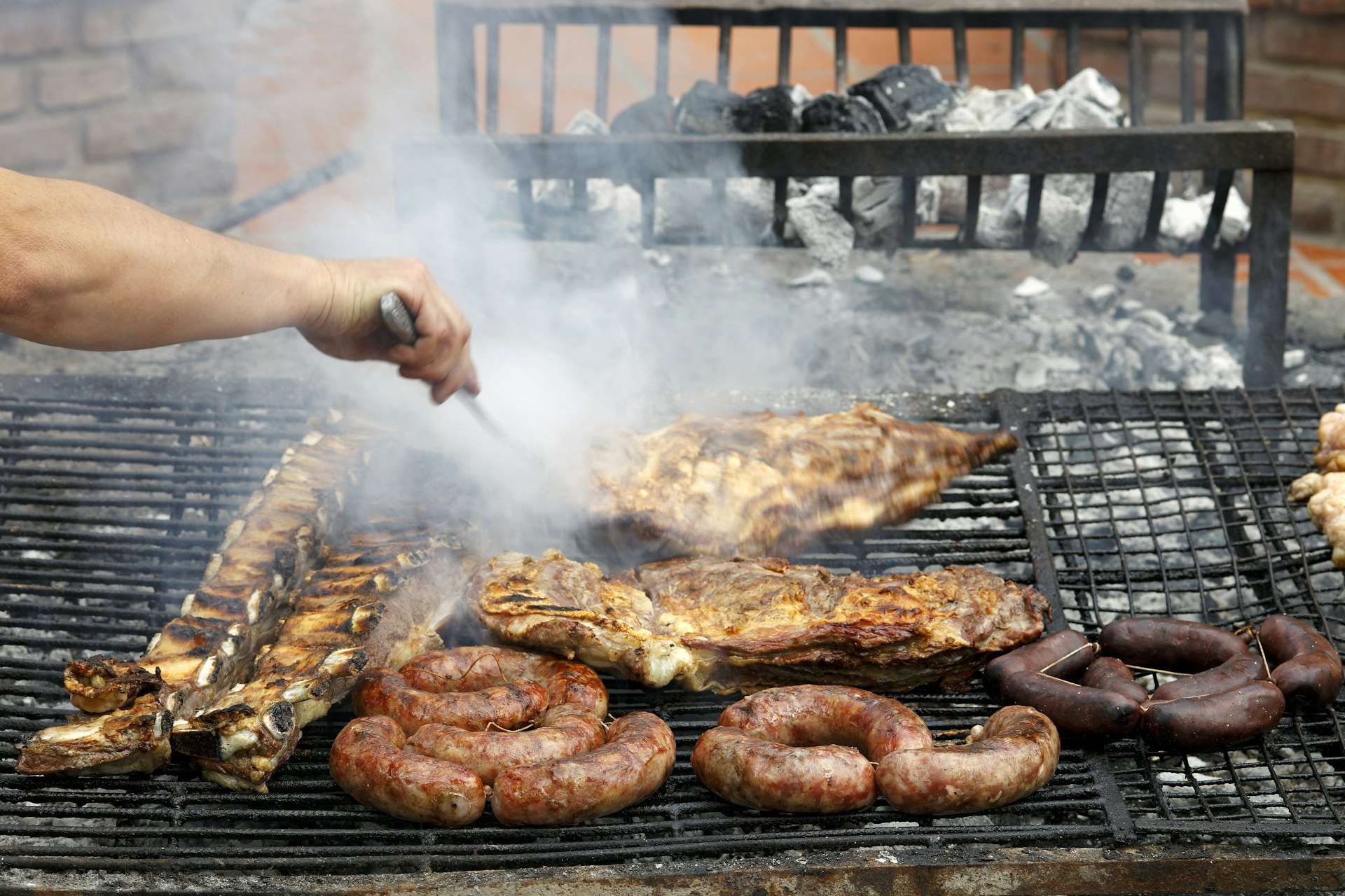 A hand turning chicken, ribs and sausage on a smoking grill