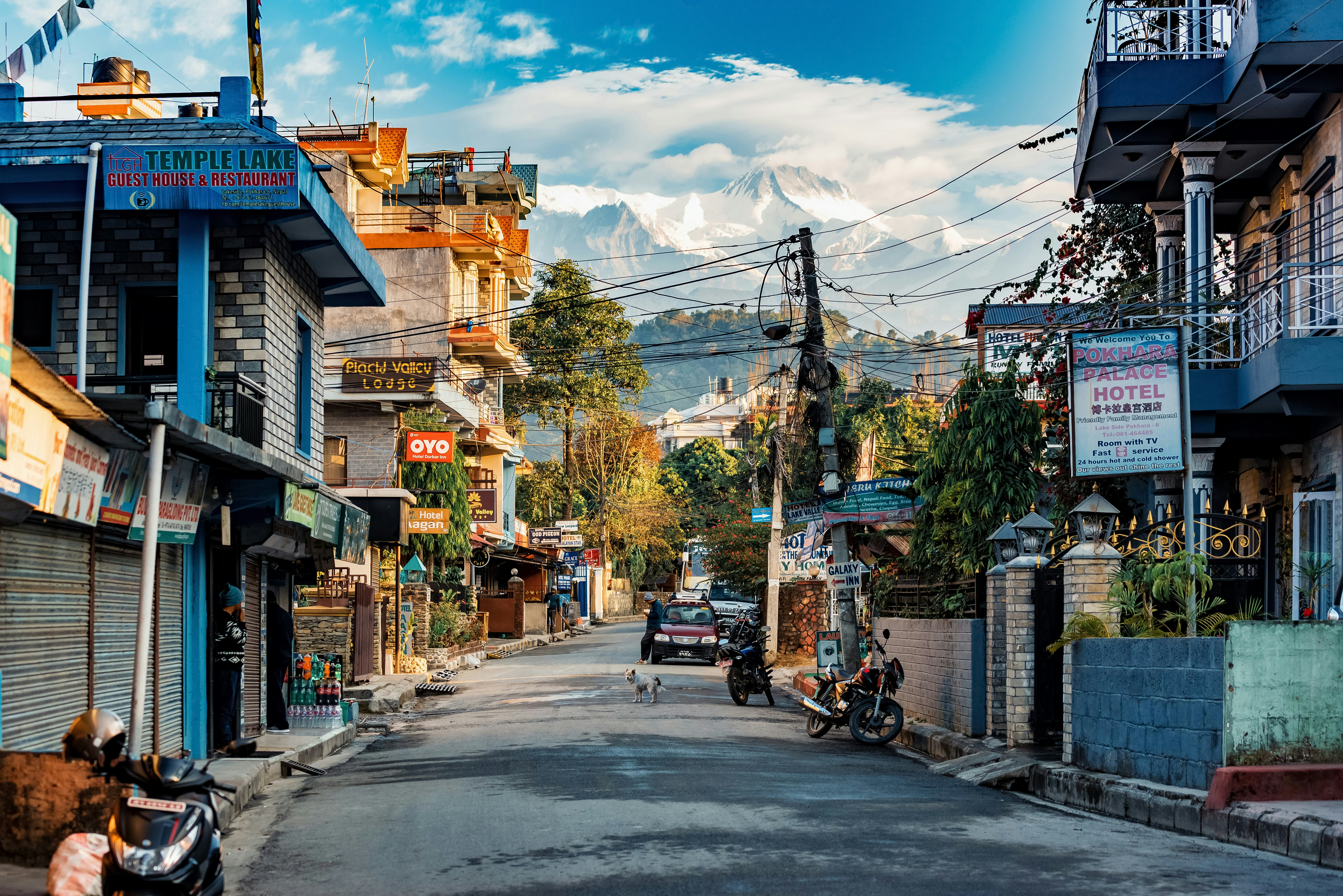 A street in a small mountain town at sunrise. Motorcycles and a car are parked beside hotels and cafes.