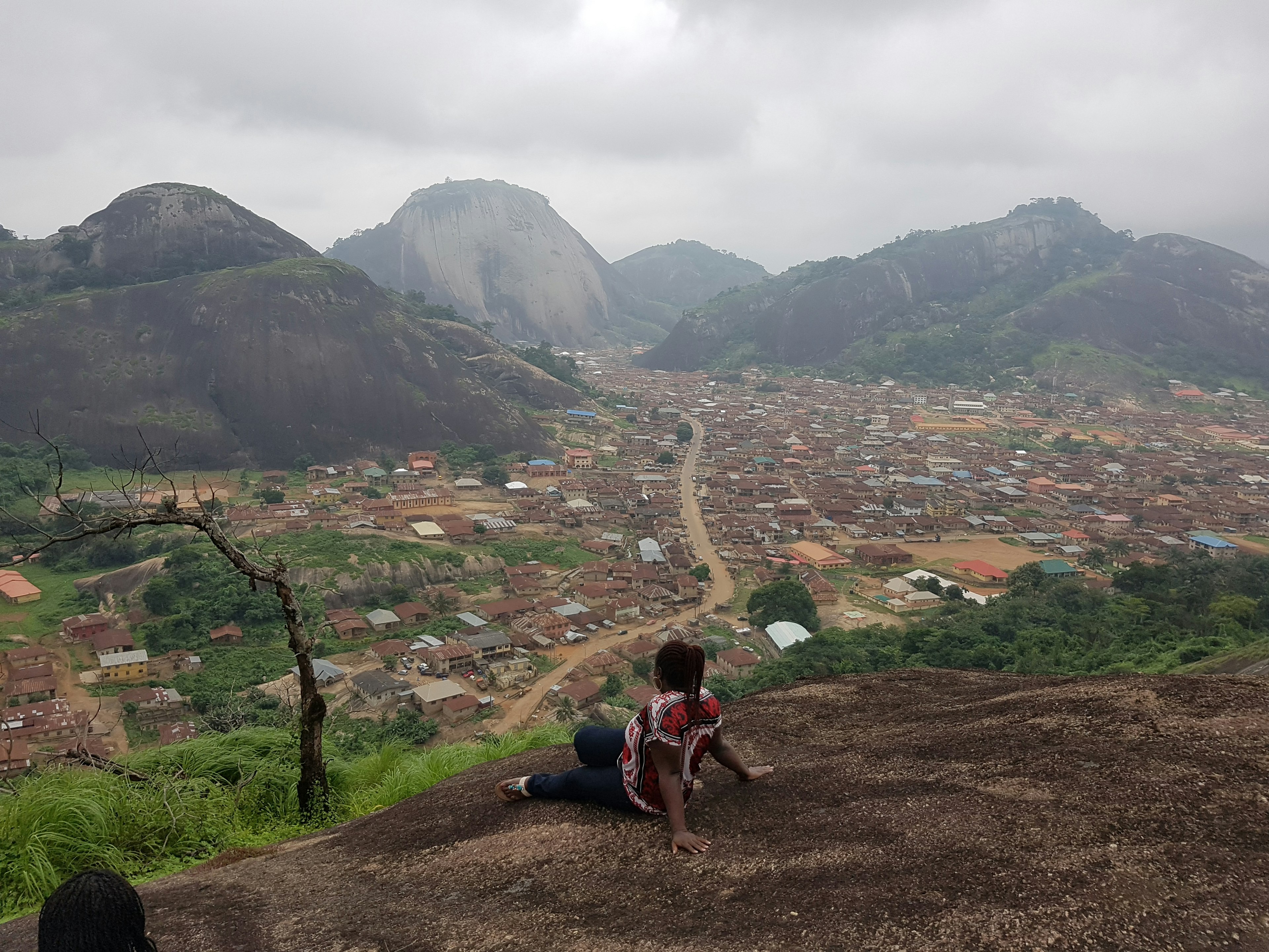 A woman sits on the edge of a viewpoint looking out to the red roofs of the settelments below the surrounding hills