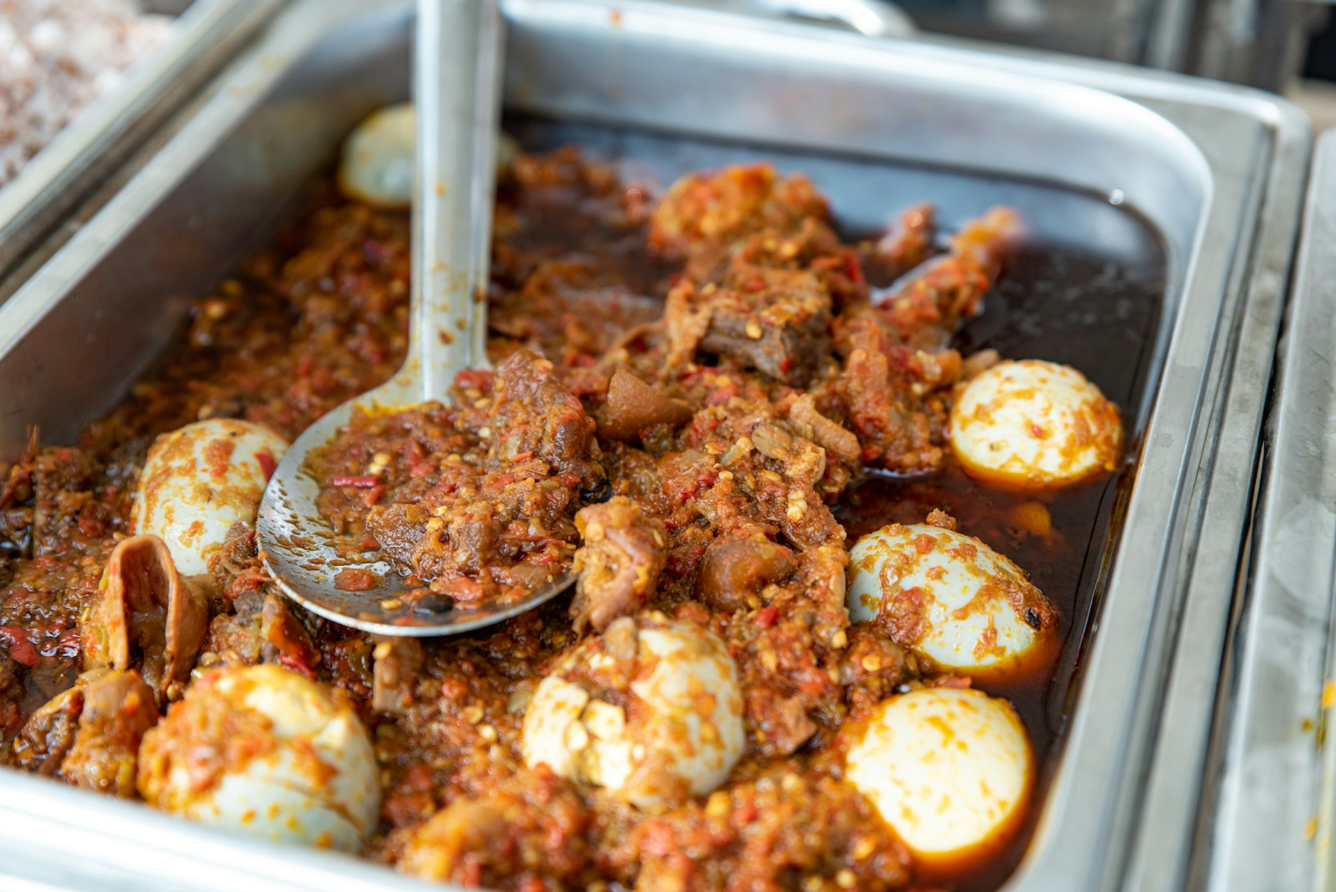 A spoon sits in a large dish of stew in a canteen 