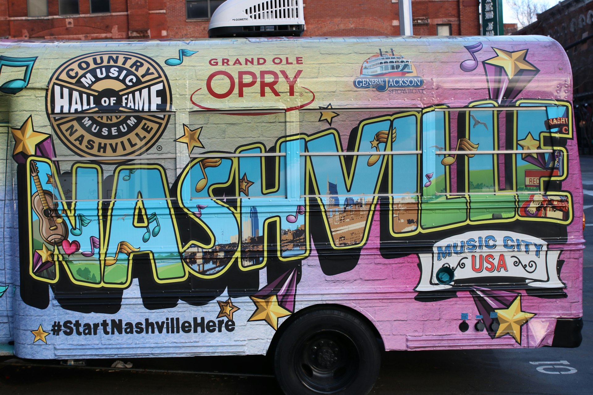 The side view of a parked bus which is emblazoned with 'Nashville' on the size parked in the city of the same name