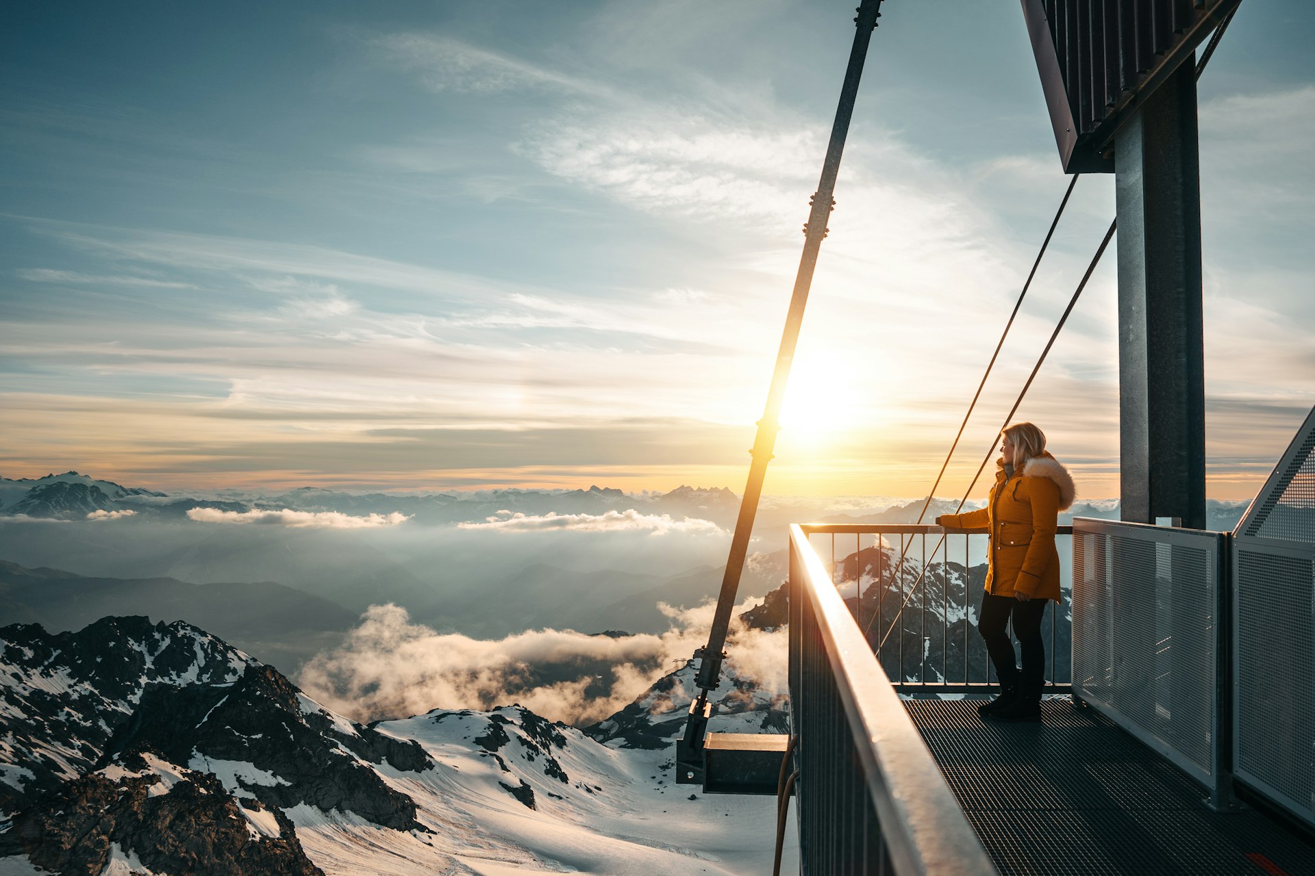 A woman on a viewing platform watches the sunrise at Mont Fort, Switzerland