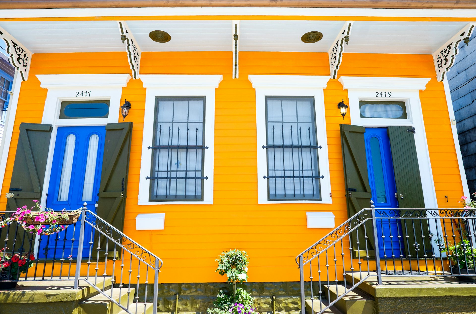 The front of a colorful historic house painted yellow with blue doors