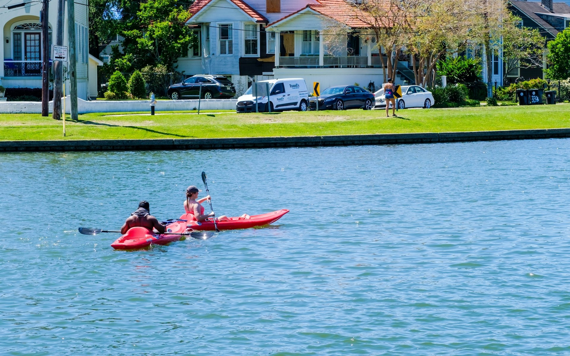 Two people in kayaks paddle down a neighborhood river