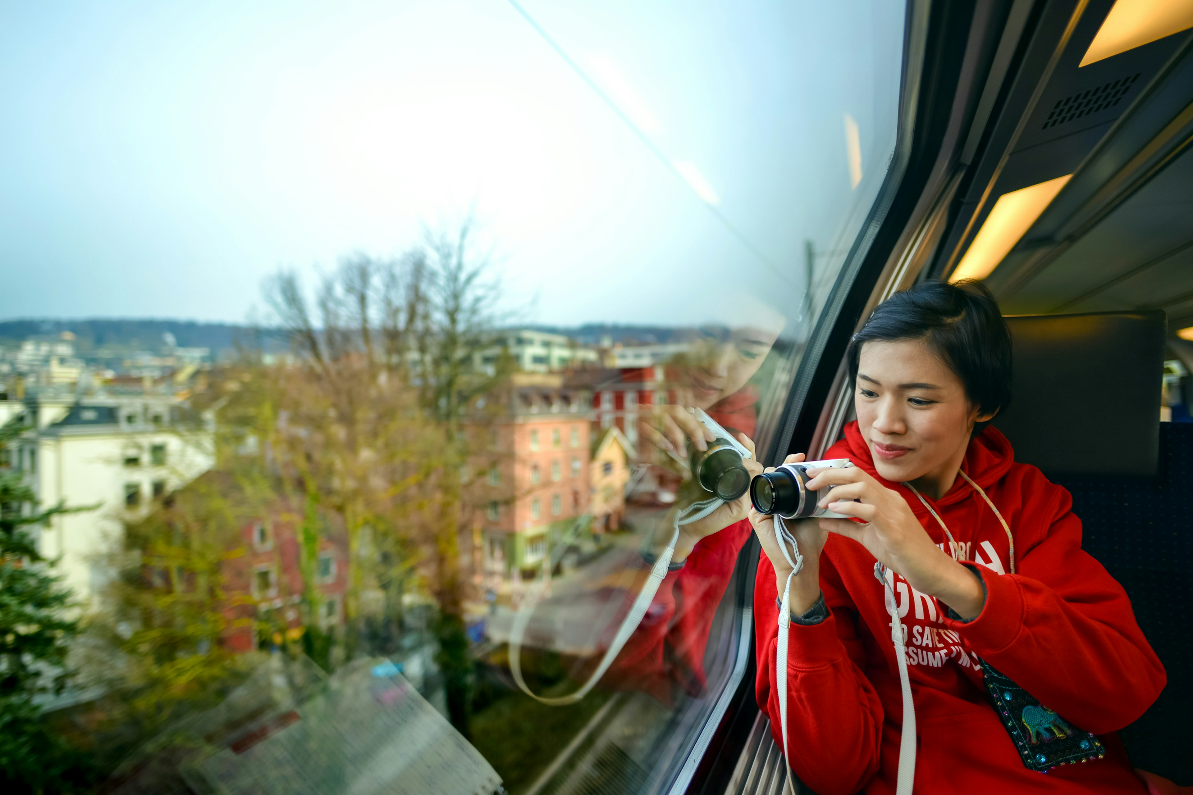 One Asian adult female visitor holding camera and looking at view through SBB train window in Zurich