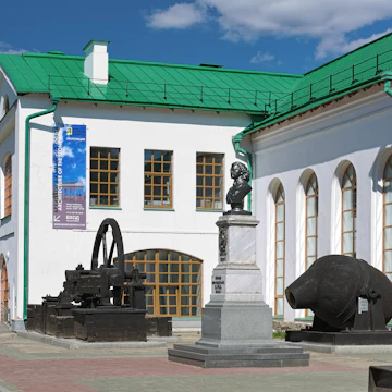 Bust of Peter I outside the Museum of Architecture and Design surrounded by iron plants equipment.
