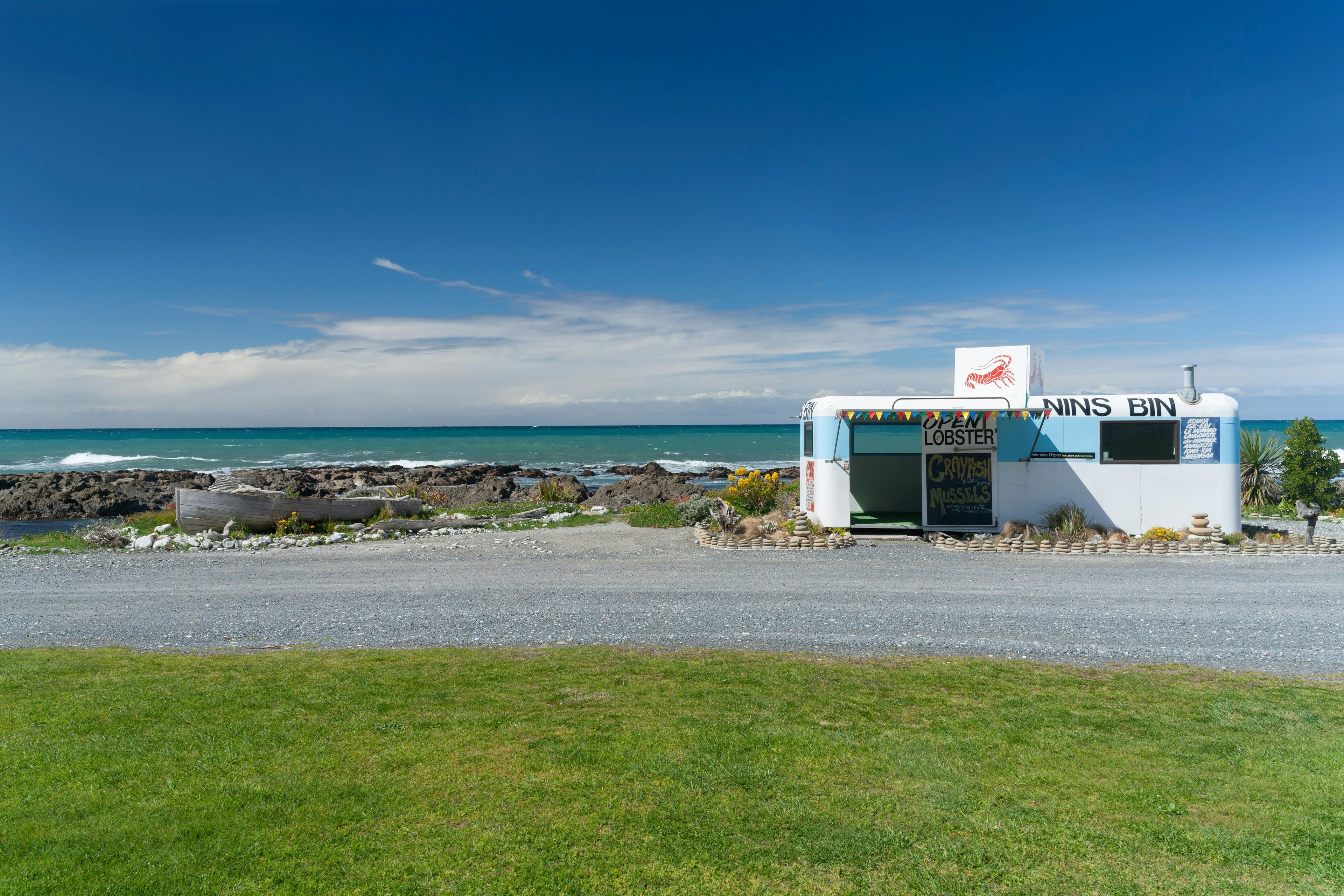 A roadside seafood restaurant in a blue truck with the coastline in the background.