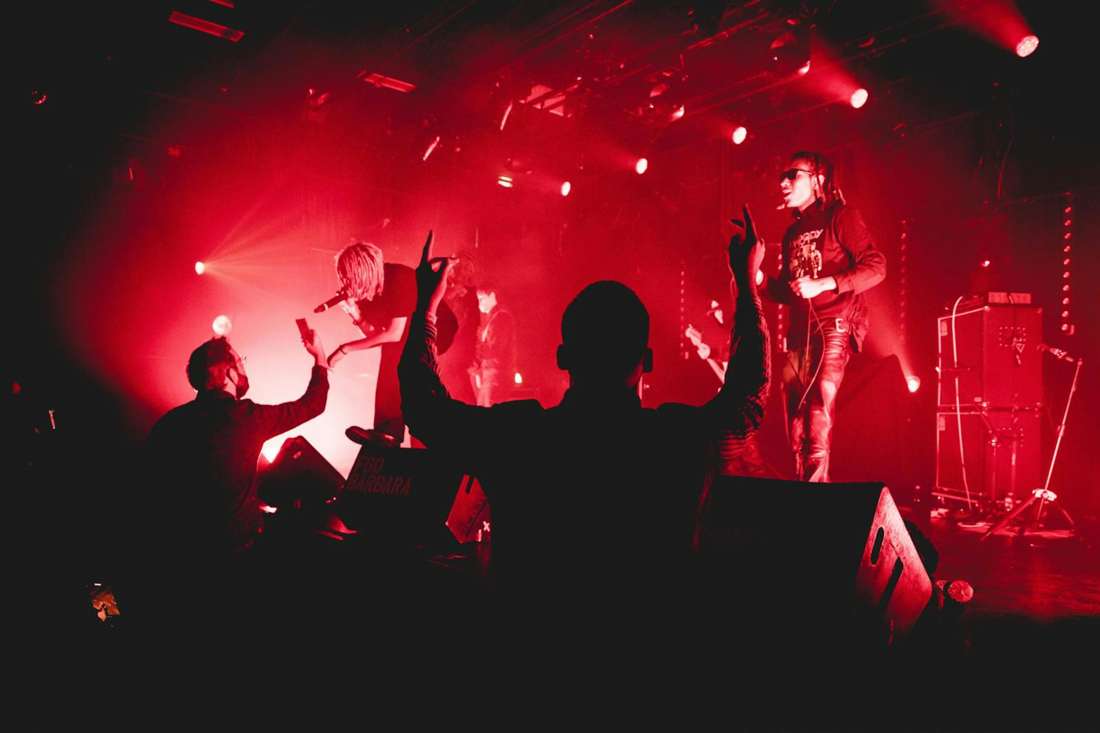 Musicians perform on stage and interact with a crowd under red spot lights