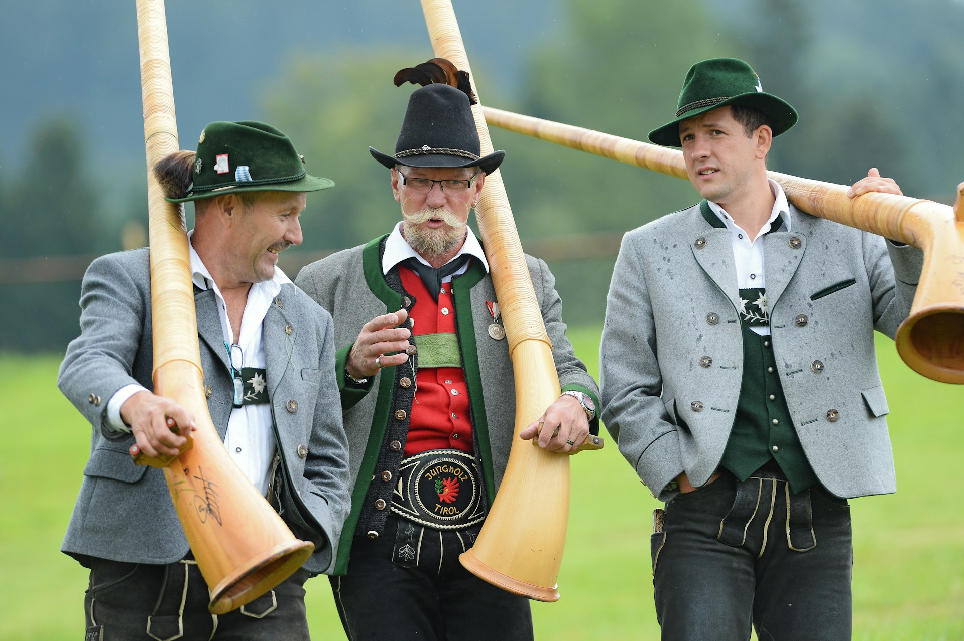 Three Alphorn blowers walk down a hill with their instruments after their performance at the Alphorn blowers meeting in Weiler-Simmerberg