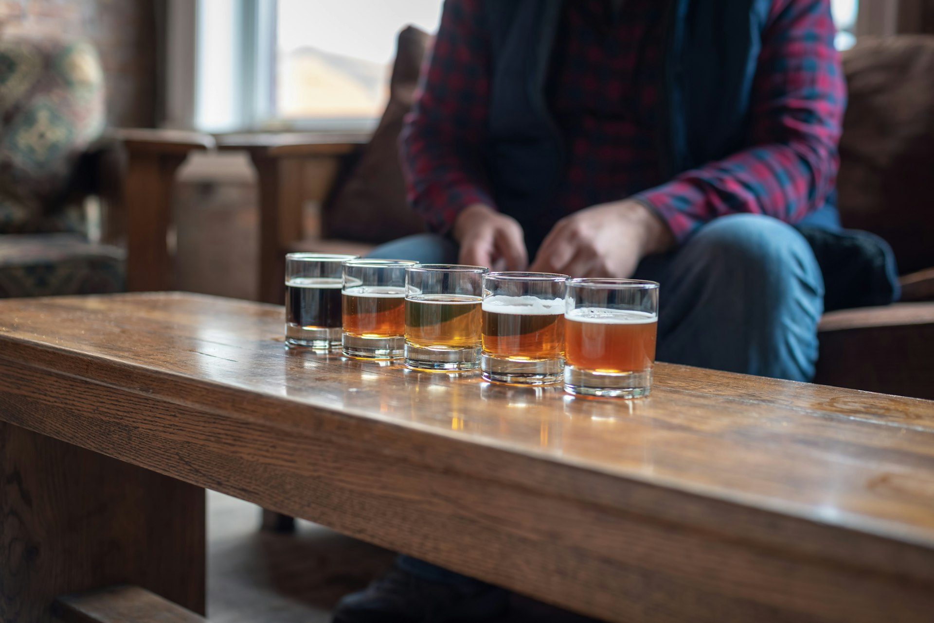 A man in a plaid top sits near a flight of beers in a microbrewery