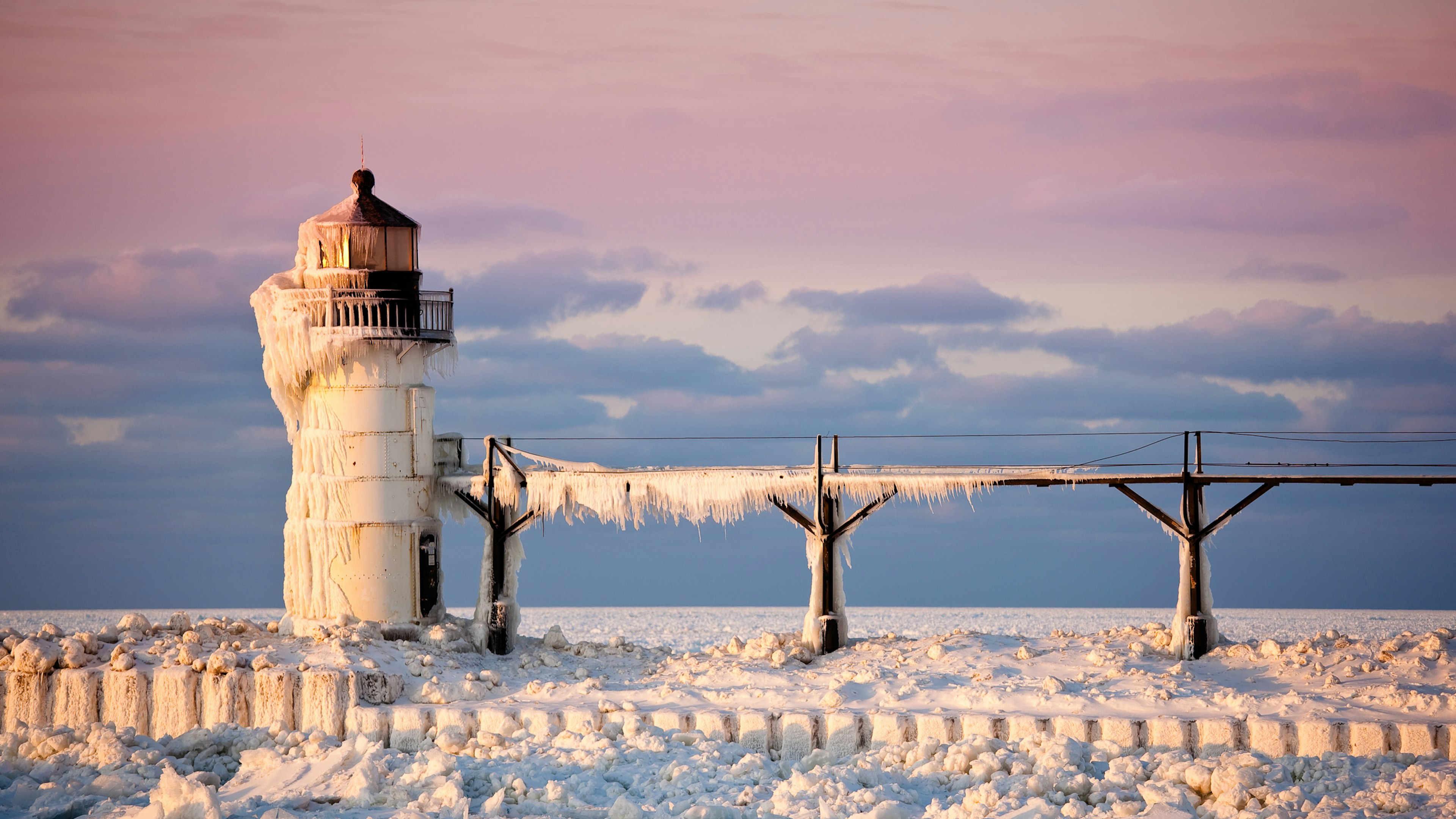 Ice and snow engulf a lighthouse on the edge of a lake