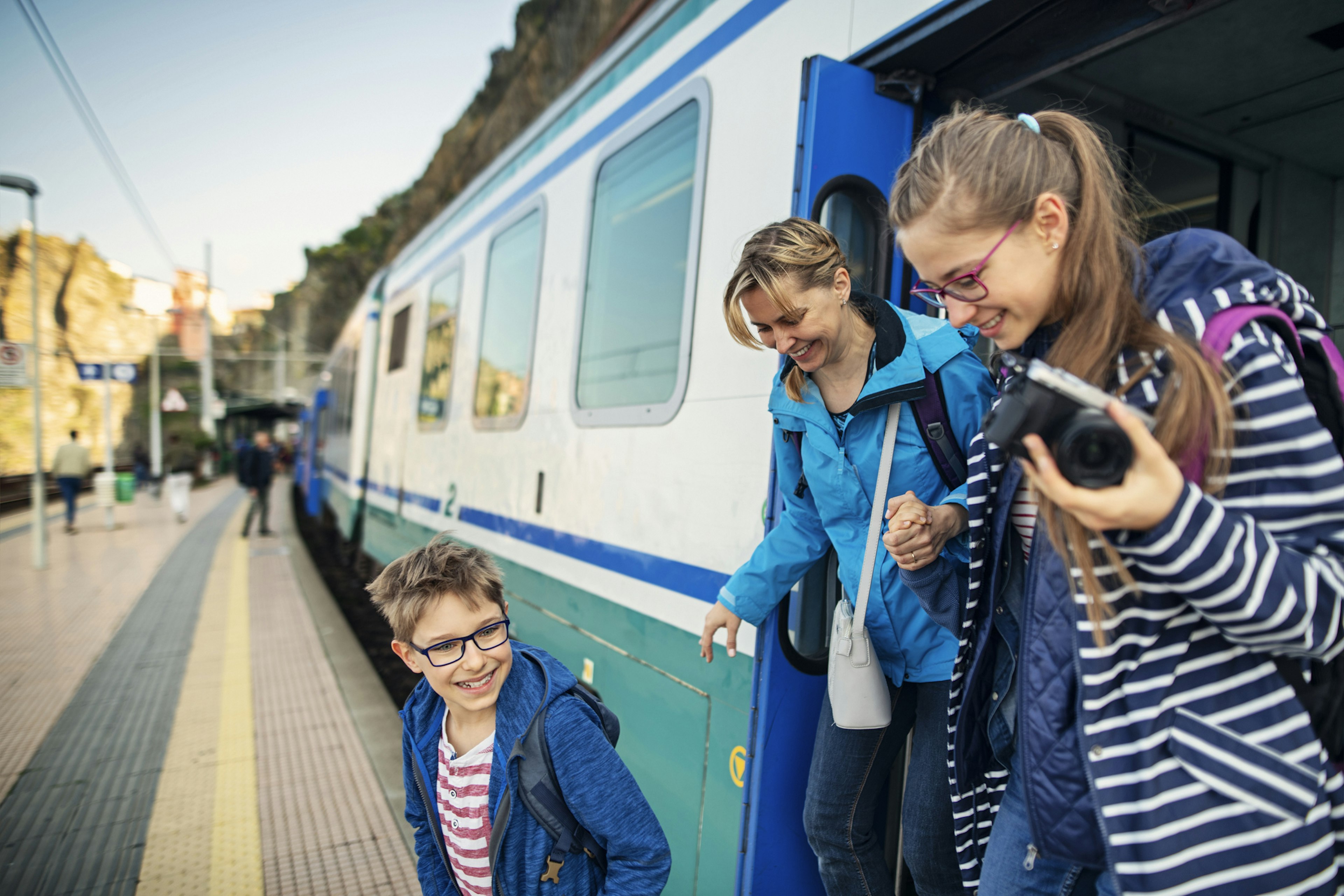 A mother and two children step off a train at a station in Italy