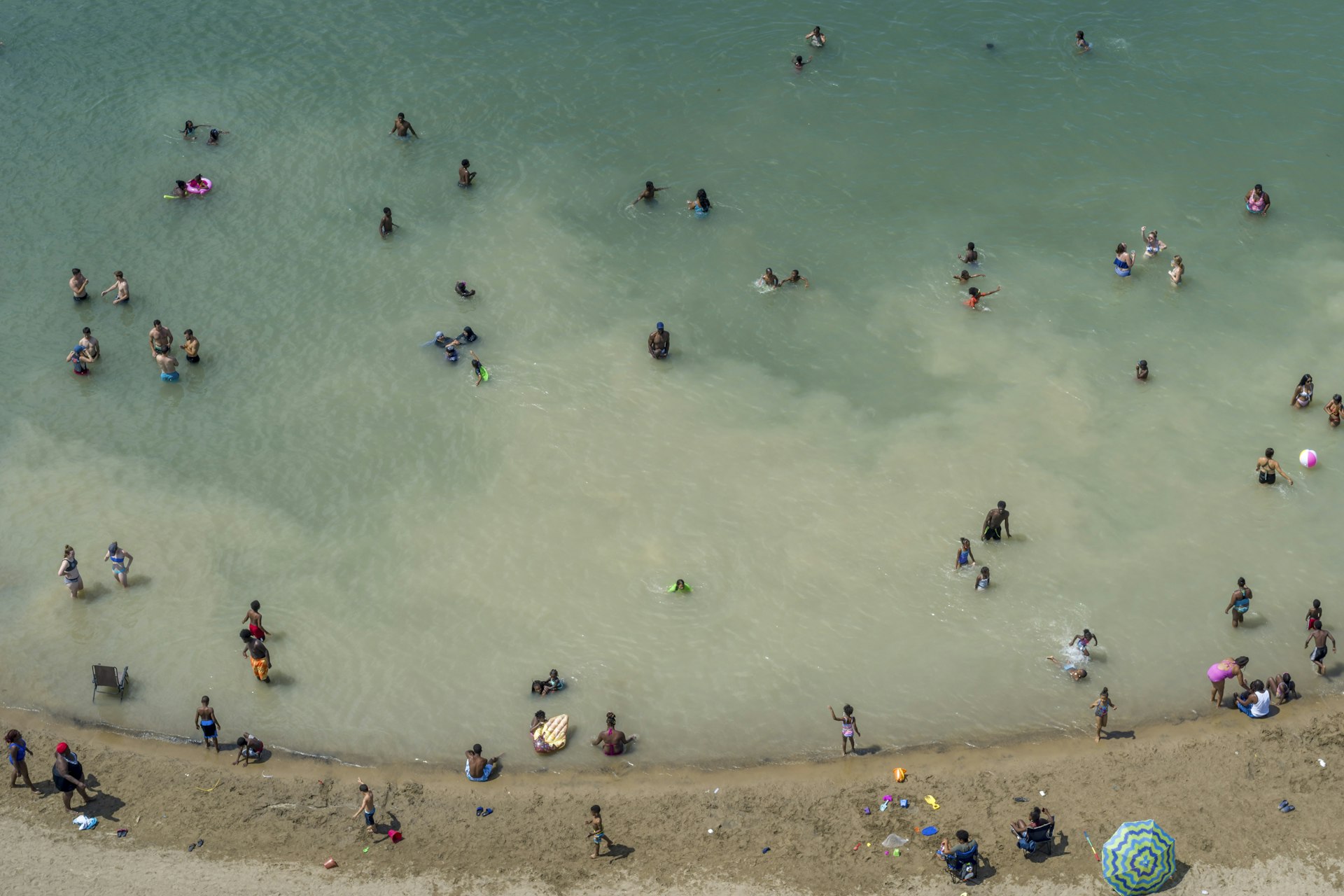 An aerial view of swimmers stirring up sediment in the muddy Detroit River on Belle Isle