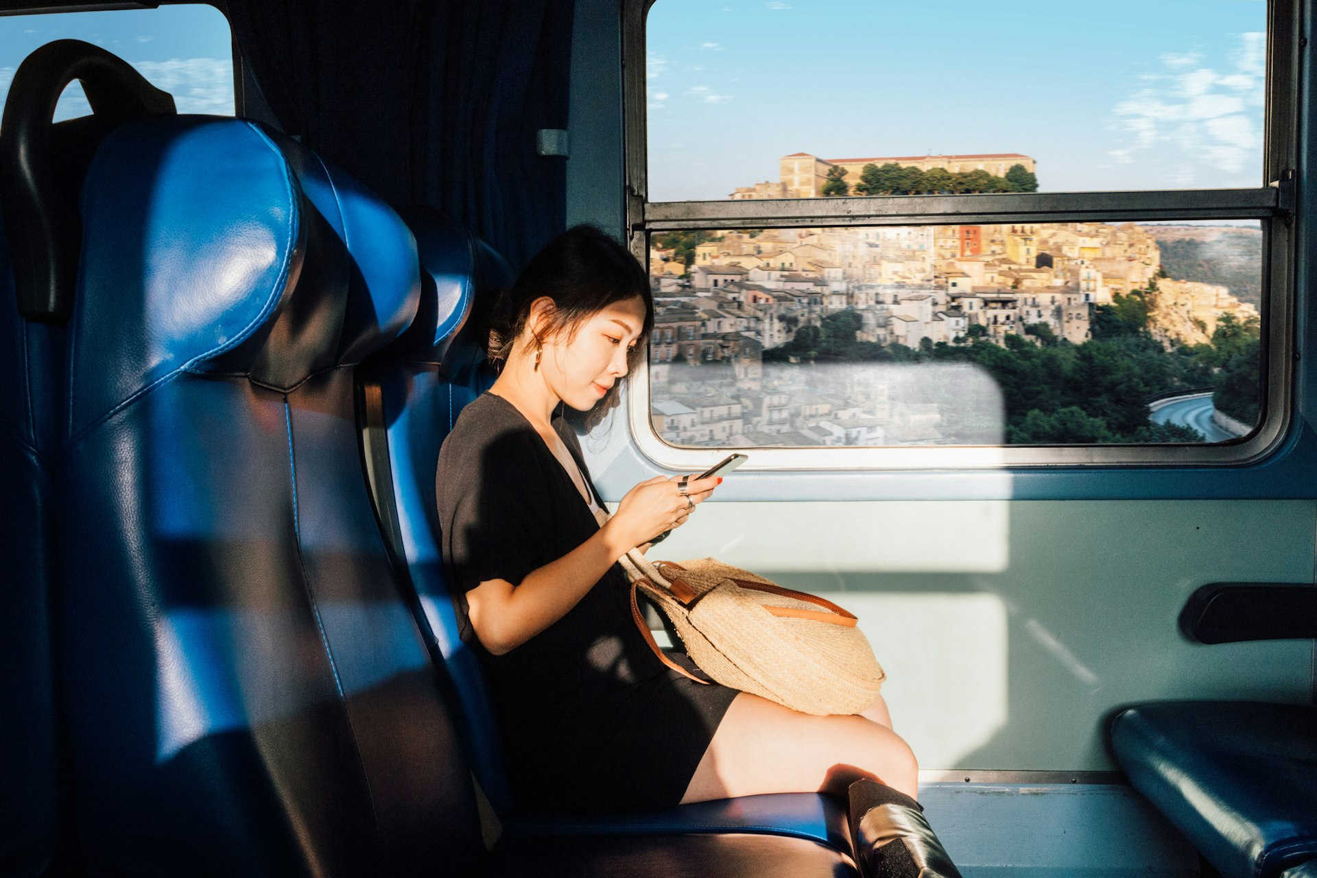 A young East Asian woman using her phone on a train in Sicily