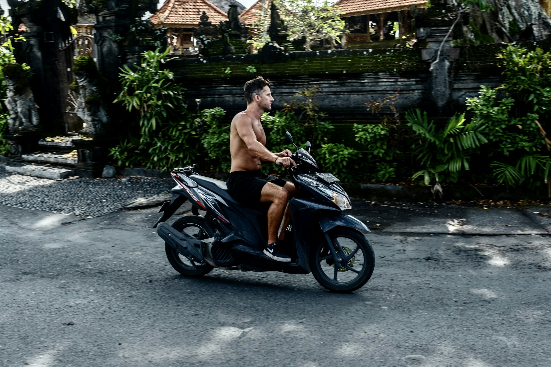 A shirtless man rides a scooter without a helmet in Canggu, Bali, Indonesia