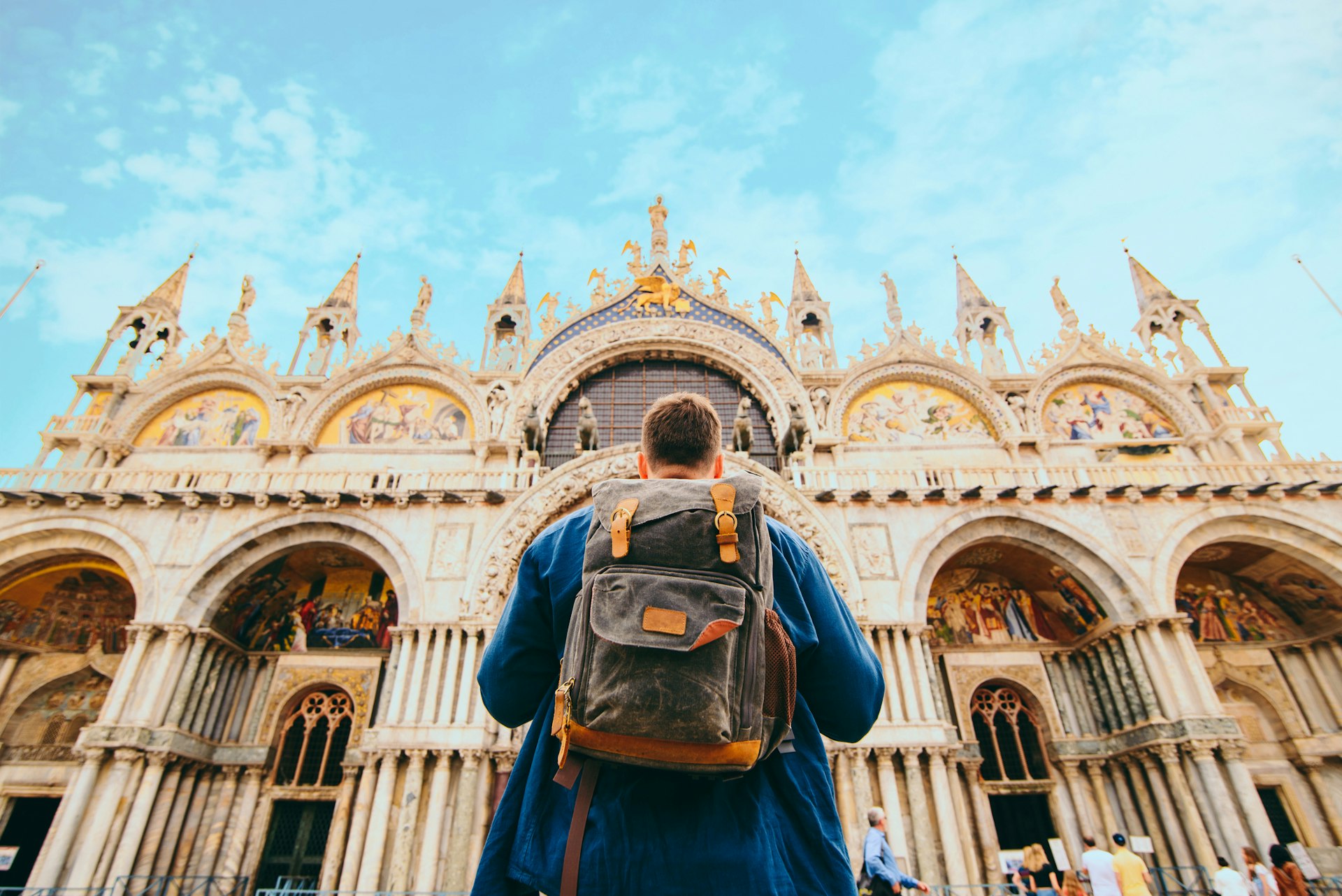 A tourist with a backpack stands in front of an ornate church facade 