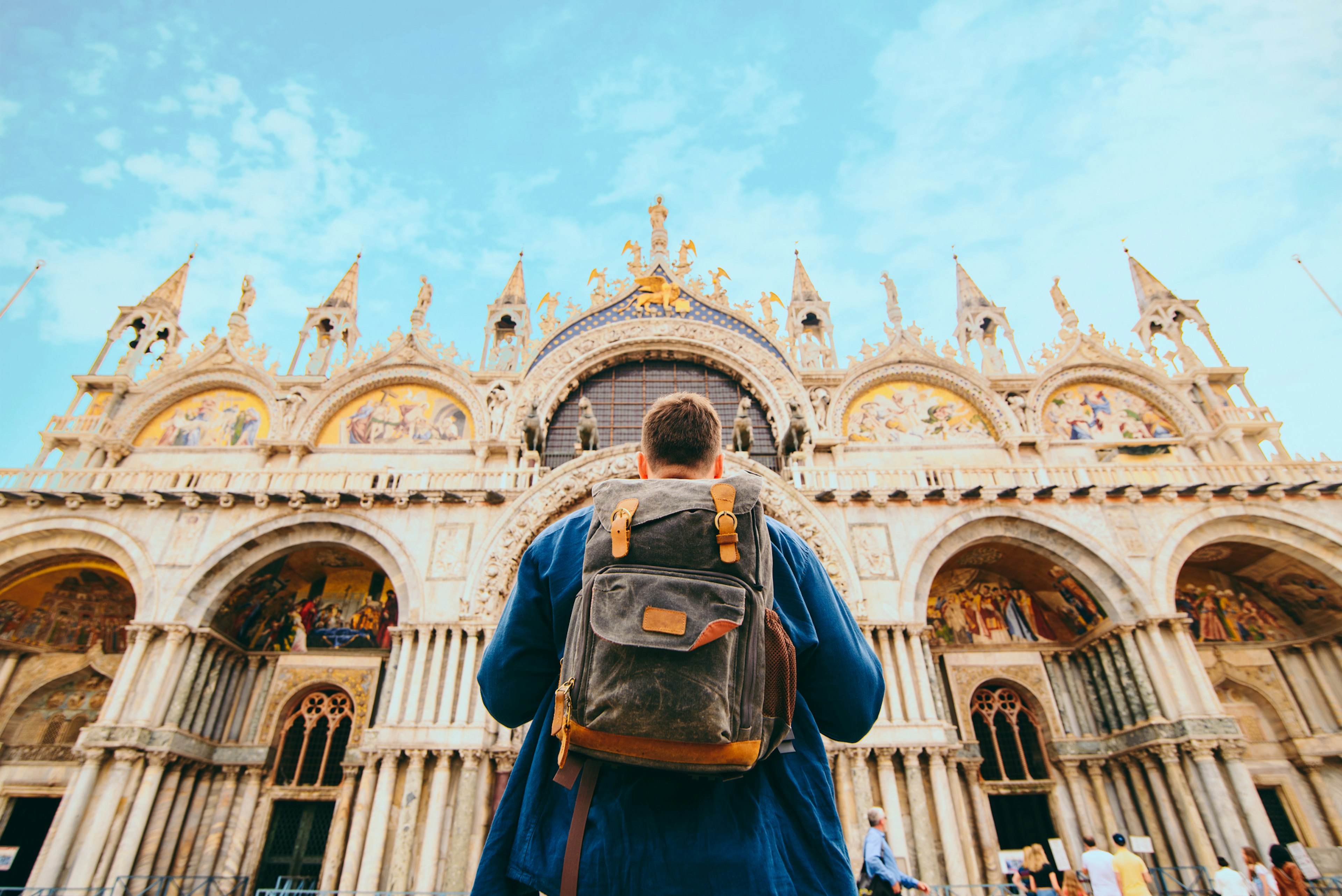 A tourist with a backpack stands in front of an ornate church facade