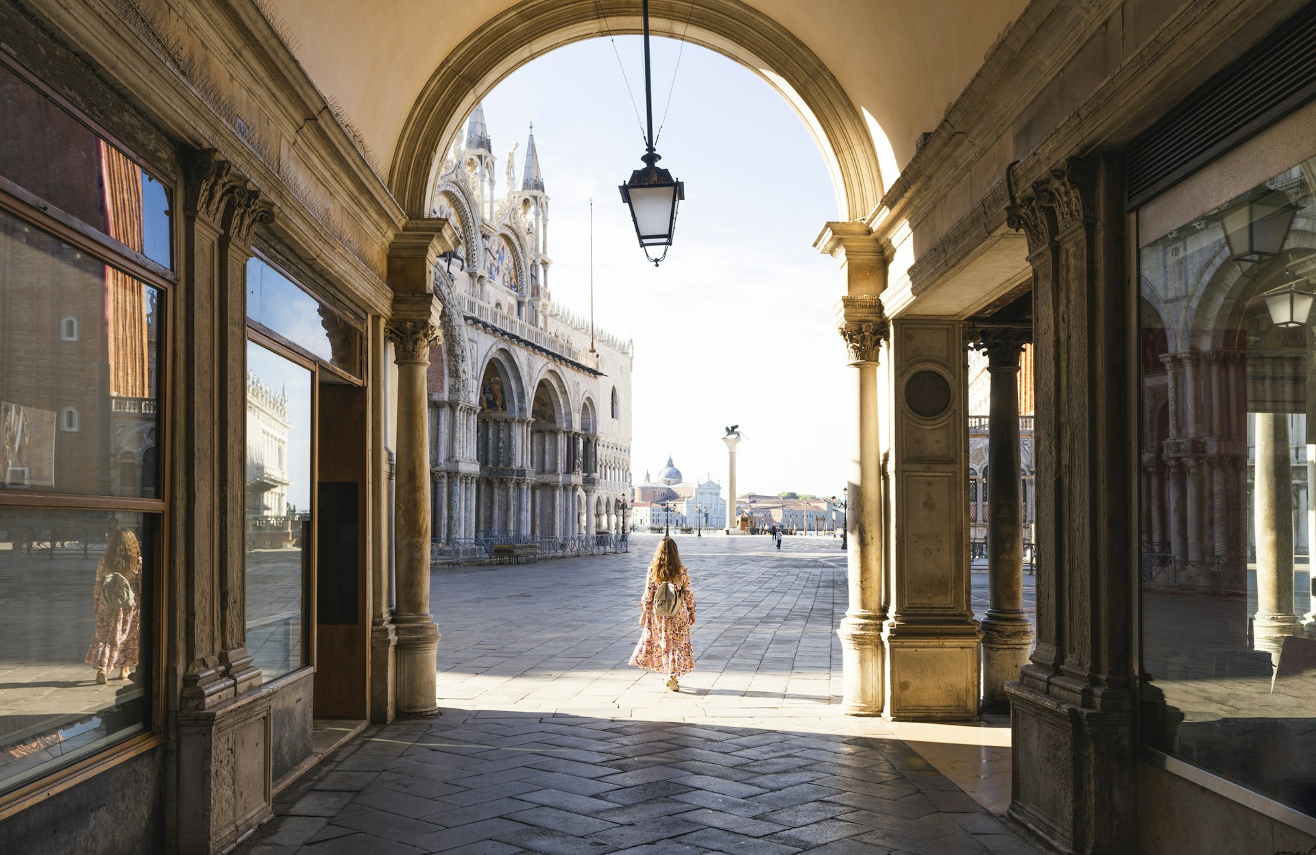 A woman walks through the arcade leading to St Mark's Square, with St Mark's cathedral in the background. Venice, Veneto region, Italy.