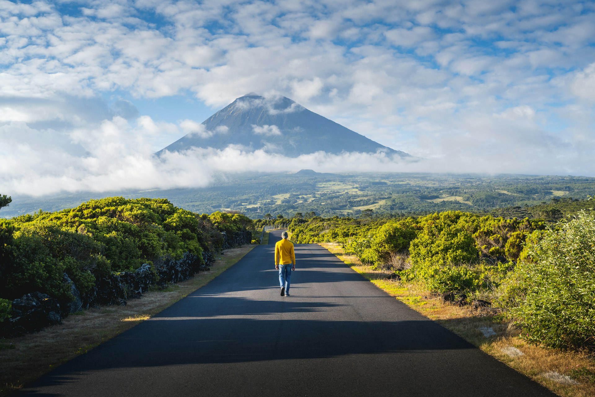 A person walking on an empty road toward Pico volcano, Azores
