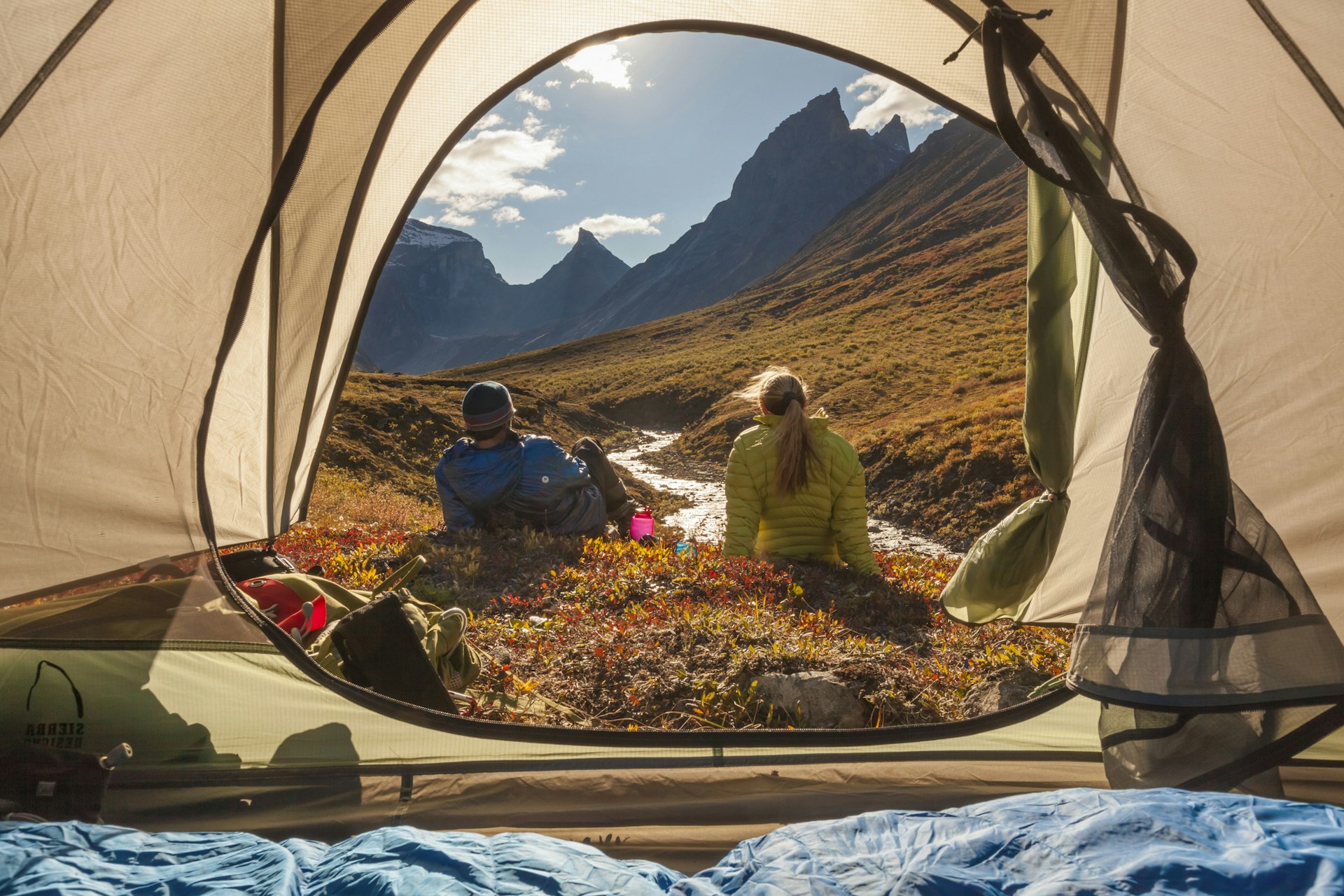 Looking out from a tent at two people sat in front of Xanadu,  Arial and Caliban mountains, Brooks range, Gates of the Arctic National Park, Alaska.