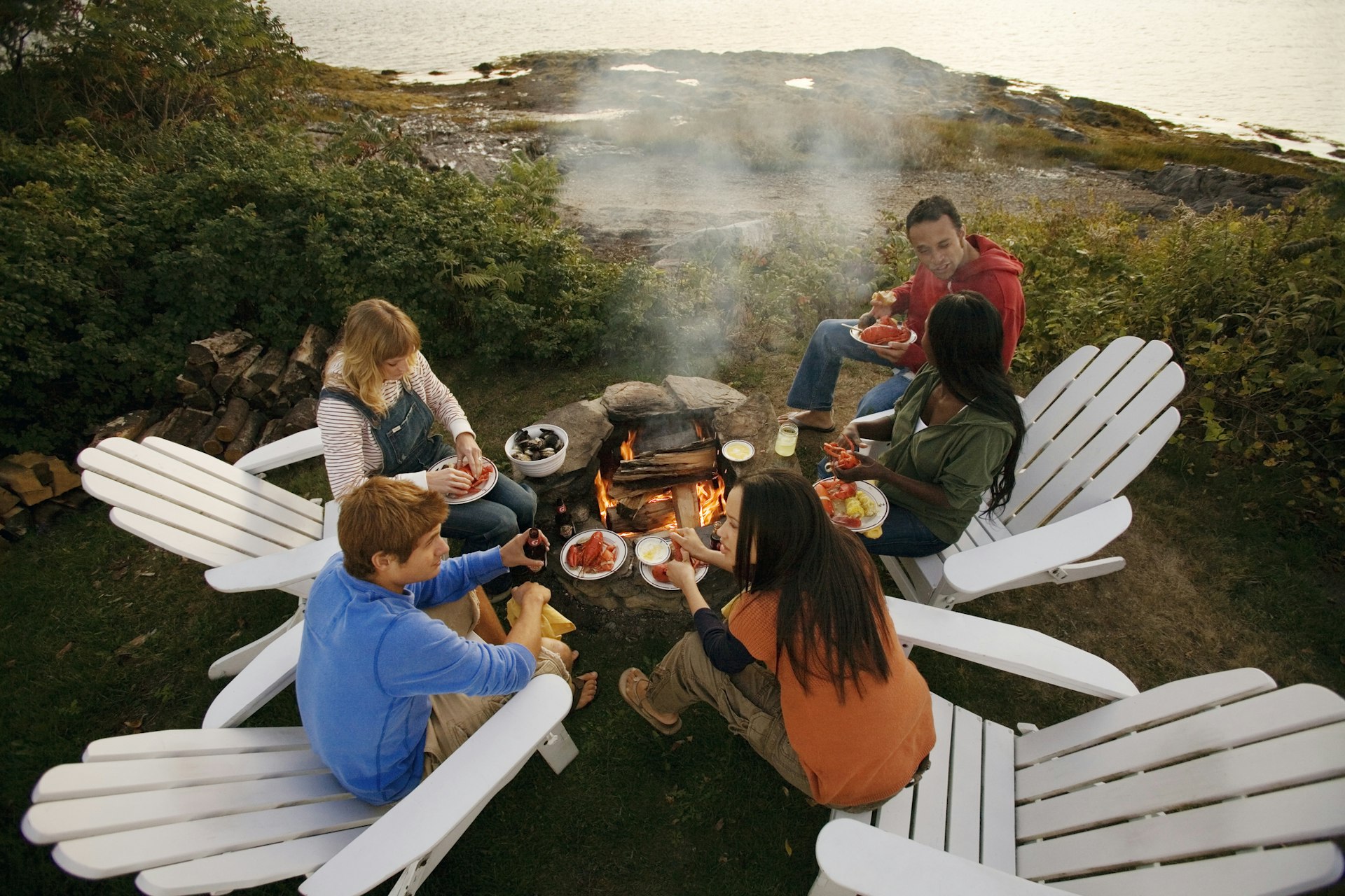 A group of friends cooking seafood over a fire outdoors in Maine