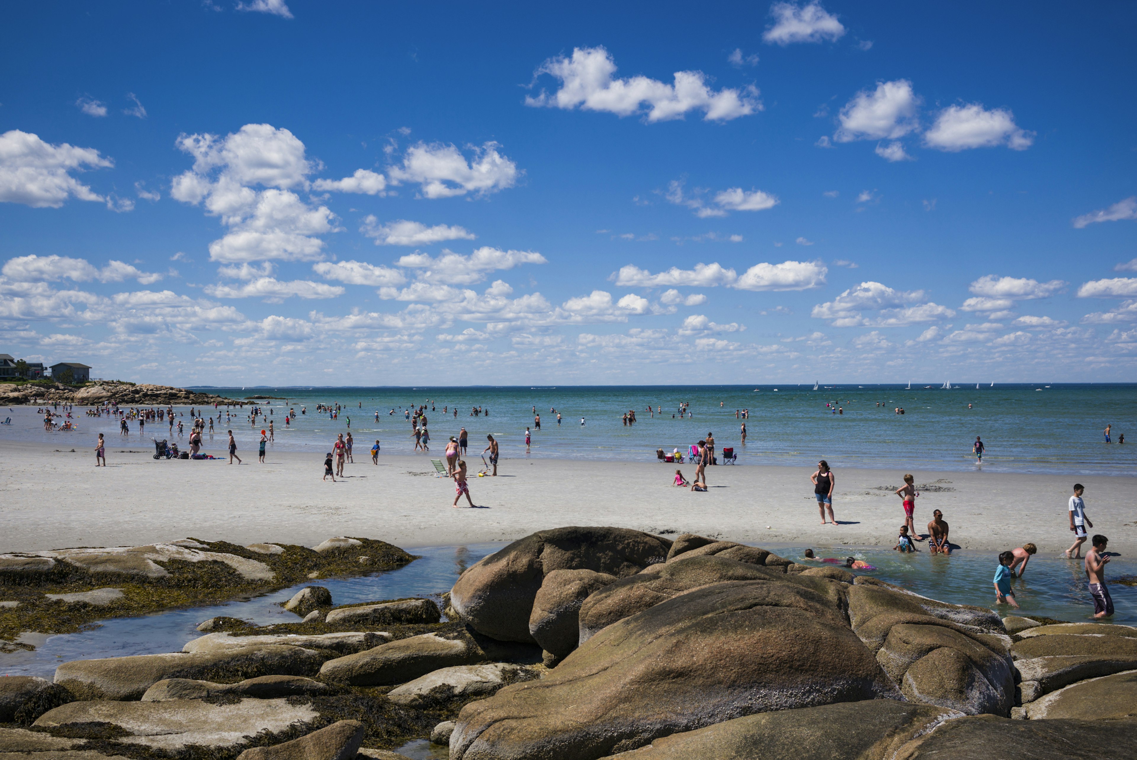 A clear ocean dotted with people enjoying a sunny day on the beach