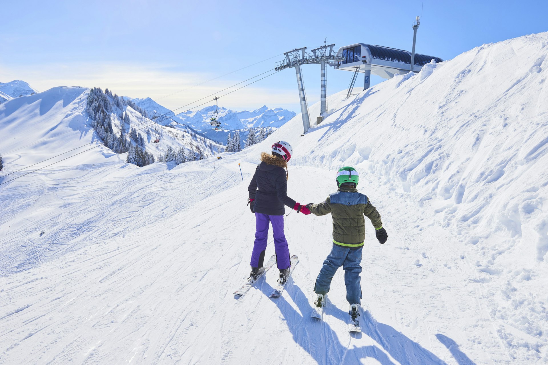 Two young children in full ski gear navigate their way towards a slope