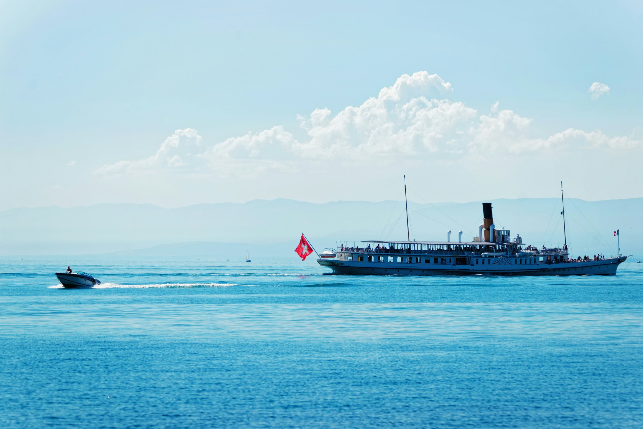 A large ferry with passengers on board sails over a lake