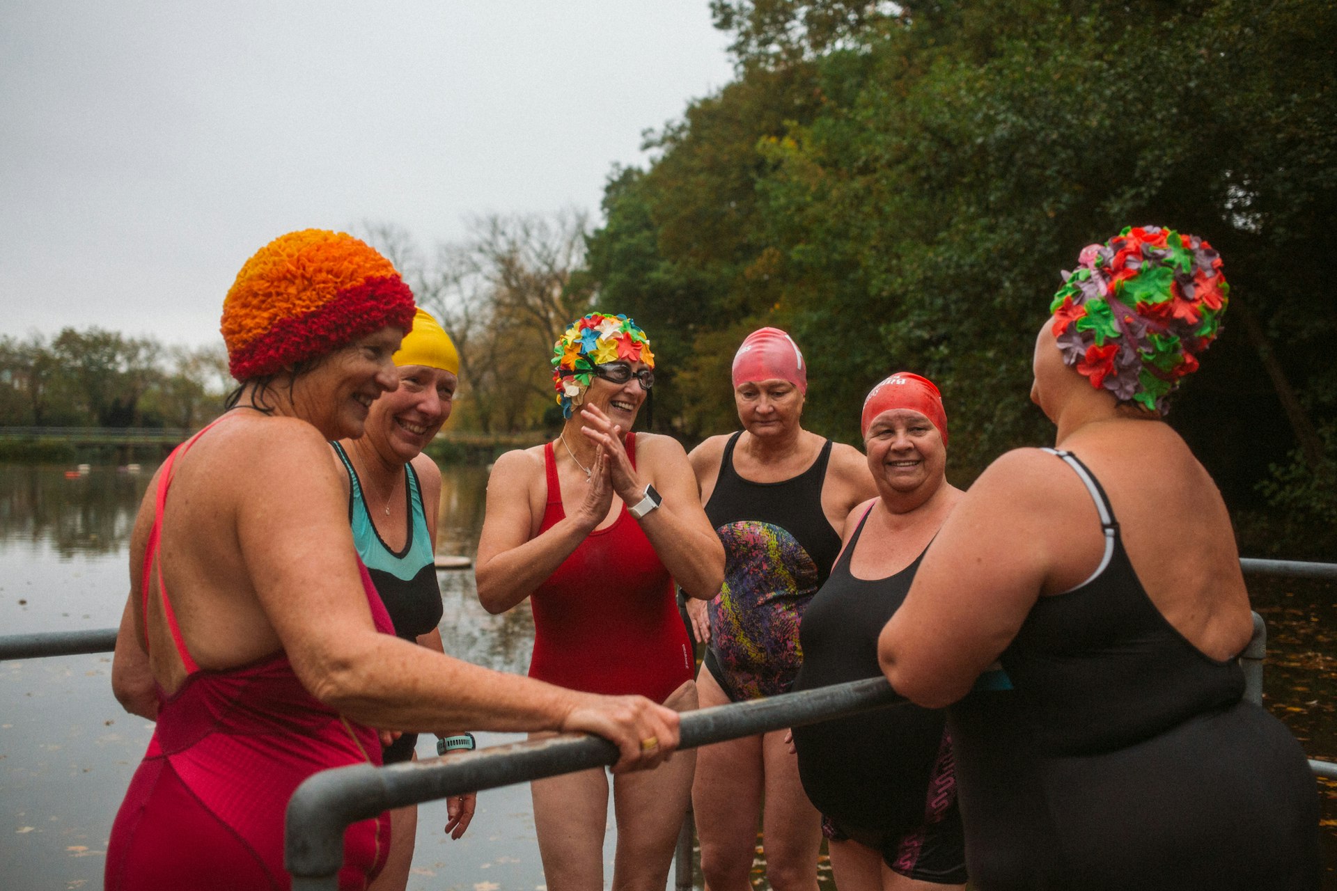 A groups of smiling women part of a Wild Swimming Women's Group take an autumnal swim at Hampstead Heath ponds 