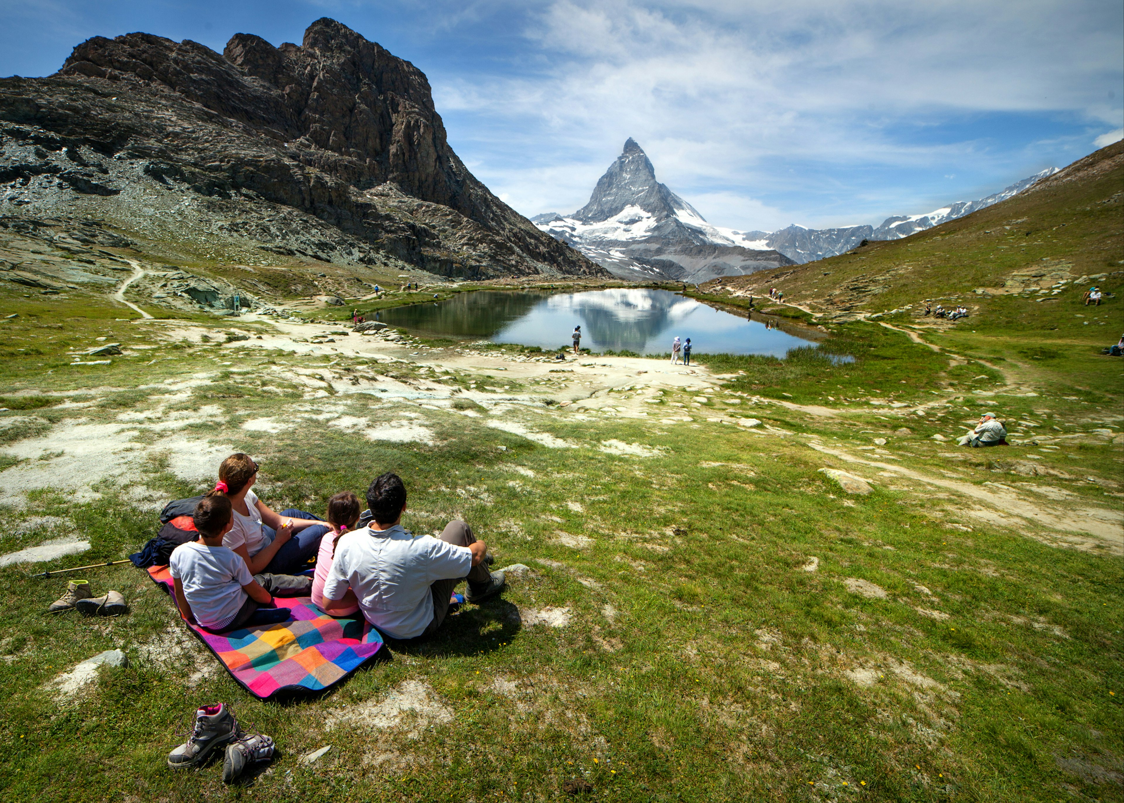 A family of four is having fun relaxing on a grassy meadow with a view of the Matterhorn in the distance